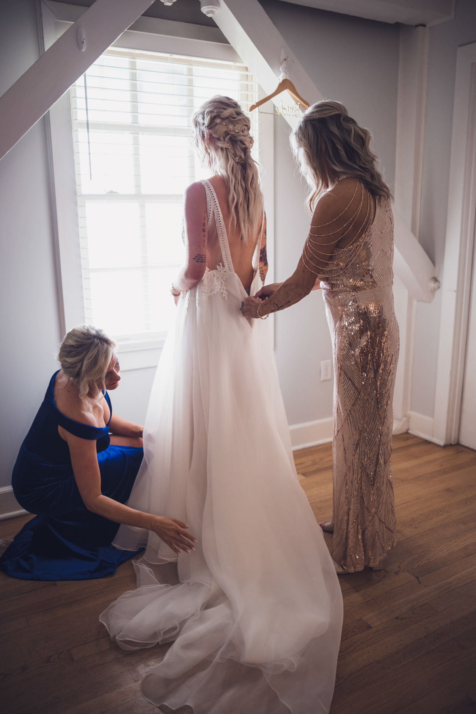 Bride getting into wedding dress with help from bridesmaids in natural window light at Alhambra Hall Mount Pleasant wedding morning