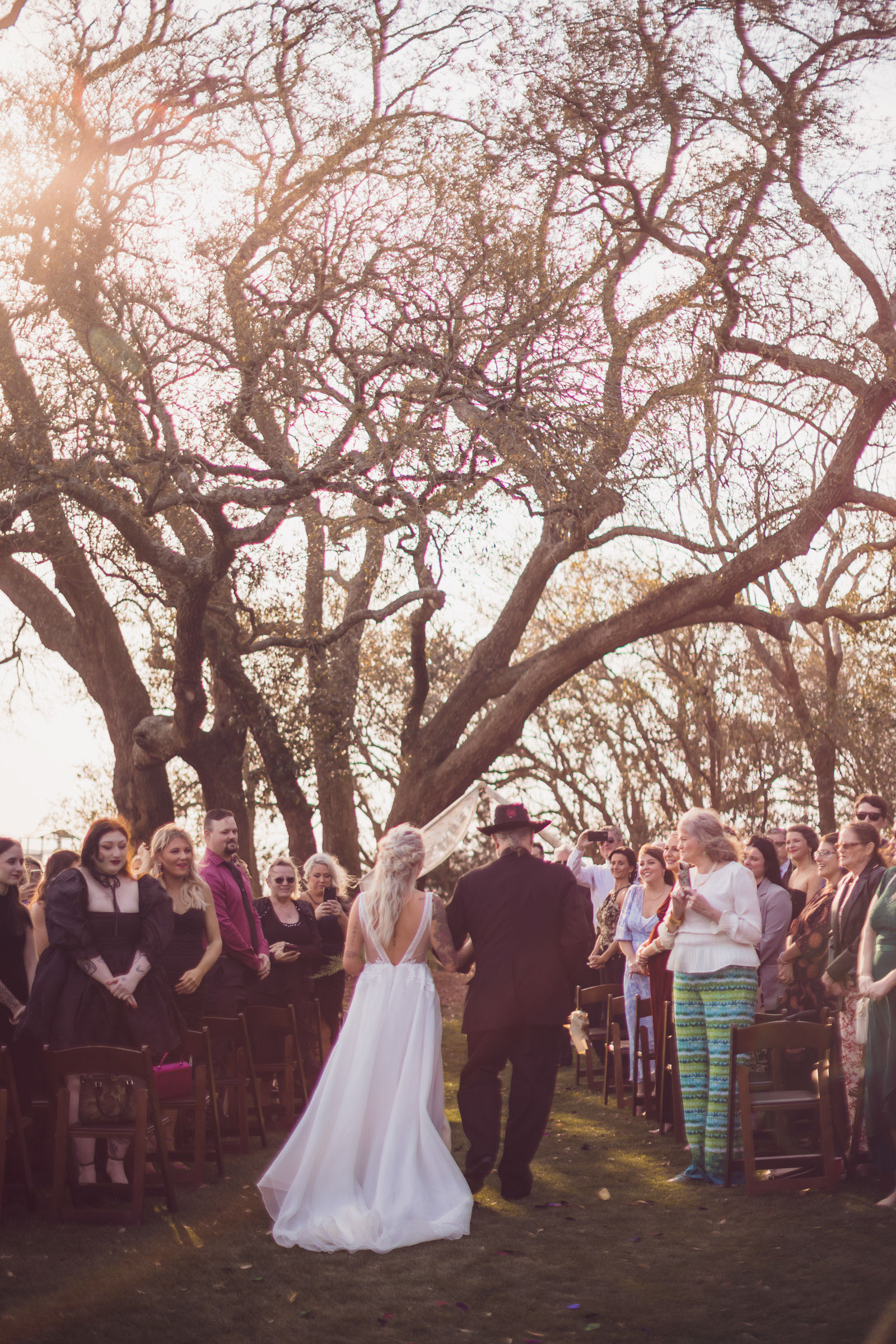 Bride walking down outdoor aisle with father under oak trees during sunset ceremony at Alhambra Hall Charleston waterfront