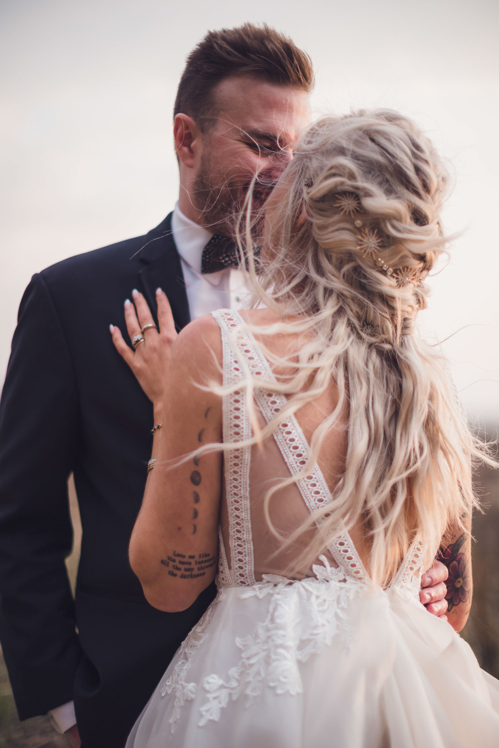 Bride and groom embracing in windy sunset light with bride’s hair blowing and lace-back wedding dress at Alhambra Hall waterfront Charleston