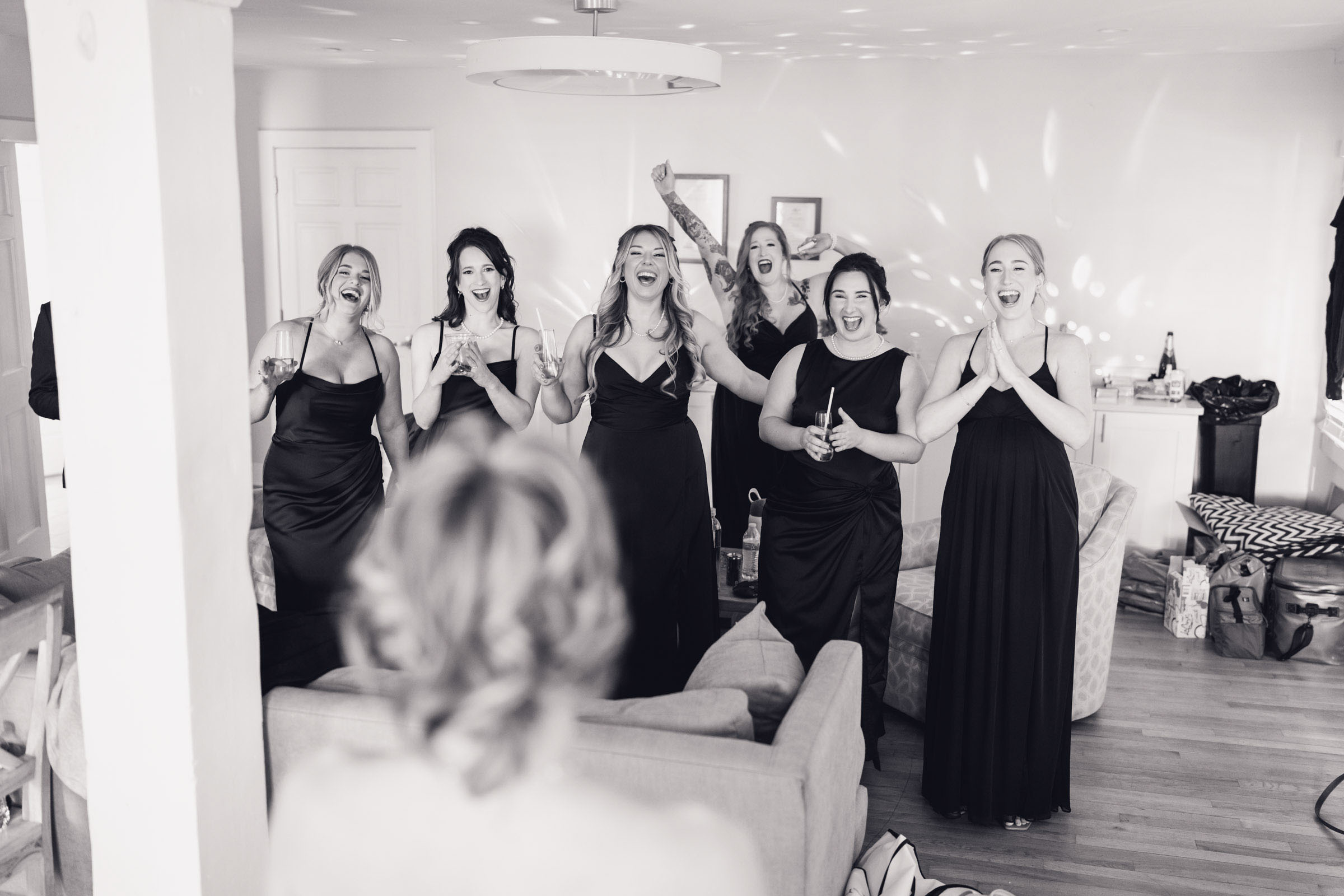 Bridesmaids in black dresses reacting and cheering as bride enters getting ready room at Alhambra Hall