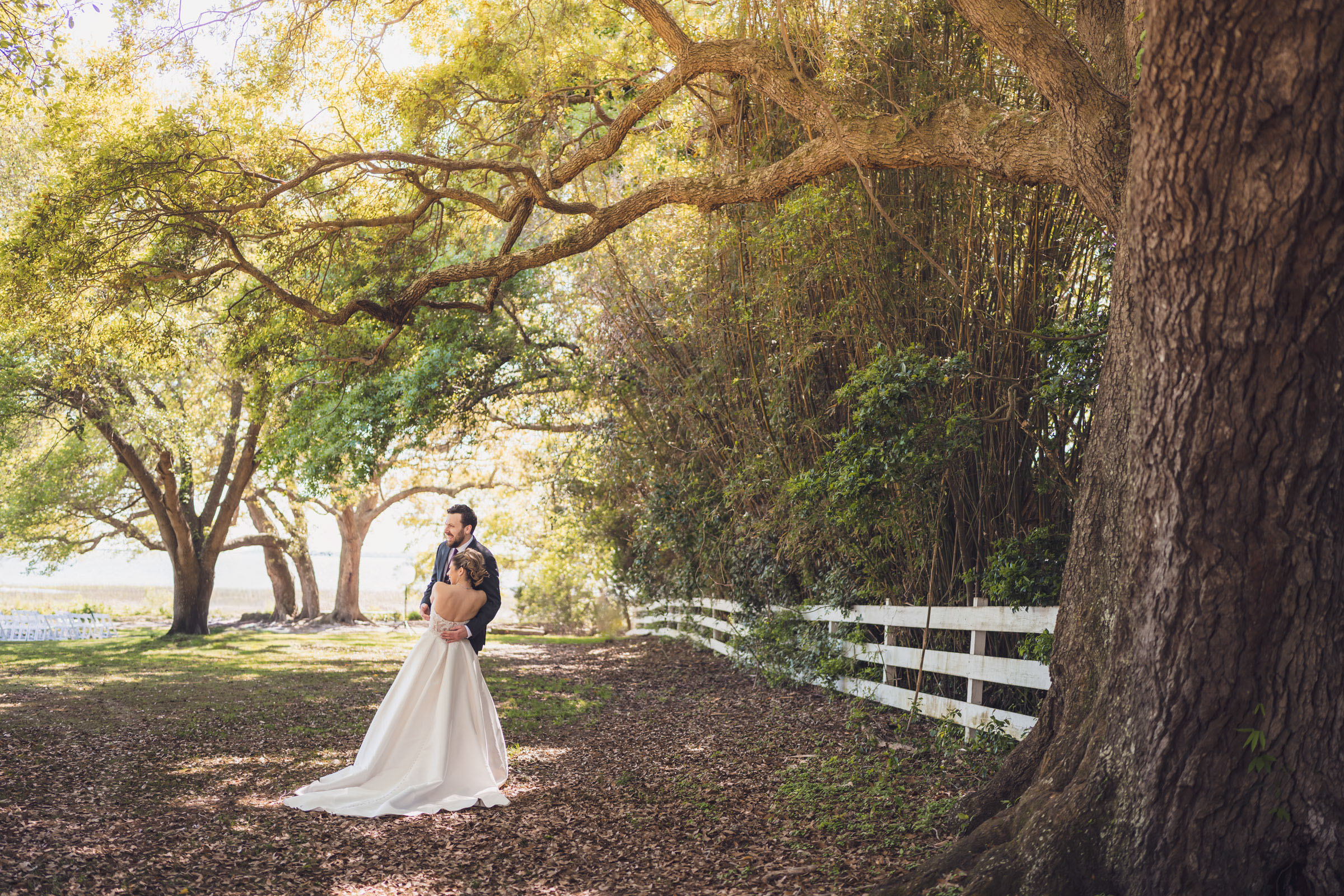 Bride and groom embracing under large oak trees by the water at Alhambra Hall Mount Pleasant Charleston