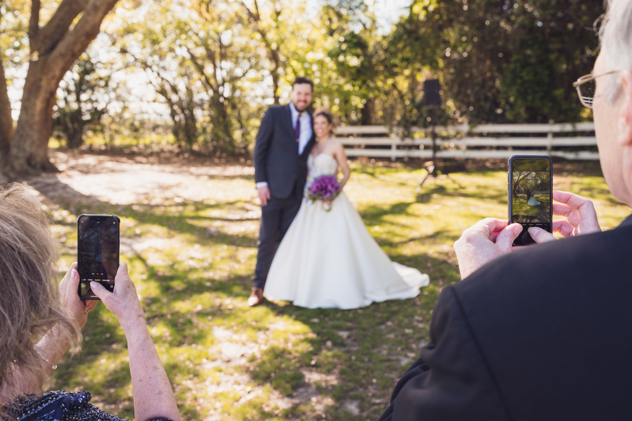 Wedding guests taking photos of bride and groom on smartphones during outdoor portraits at Alhambra Hall Mount Pleasant Charleston