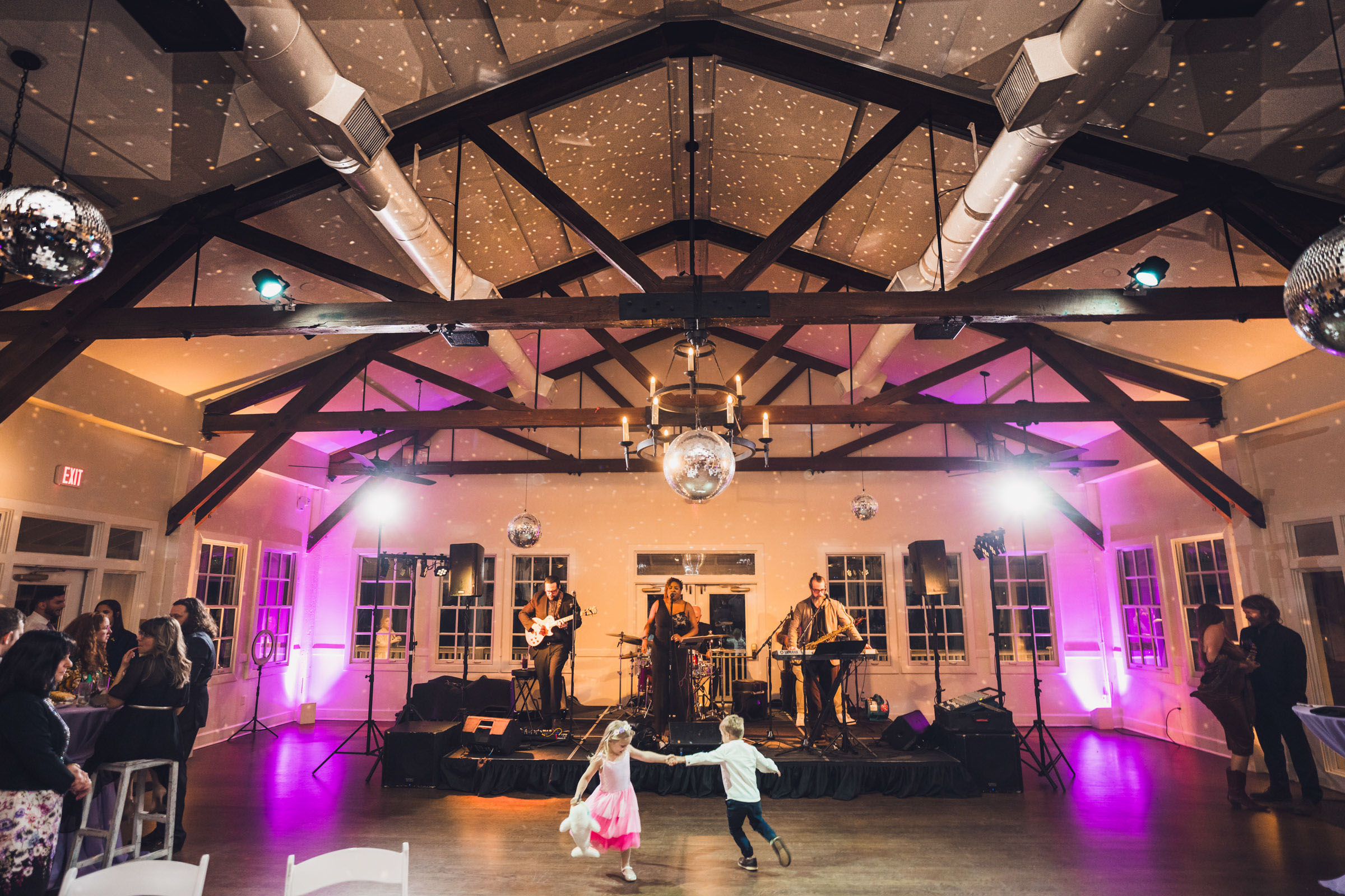 Live band performing on stage with children dancing on the floor under disco balls at Alhambra Hall