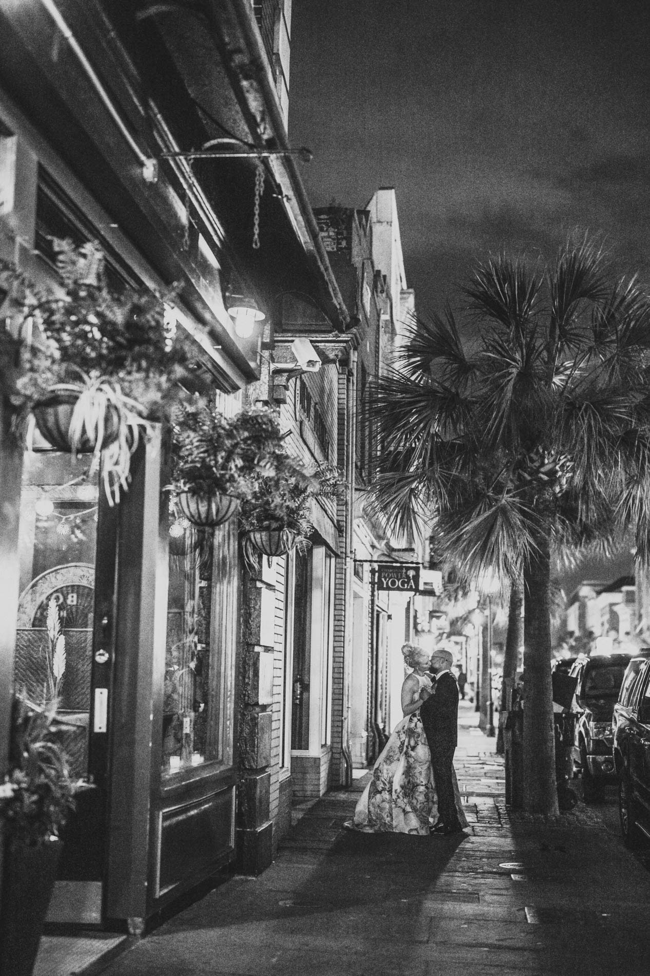 King Street Wedding Portrait Bride and groom kissing beneath palm trees during nighttime portraits on King Street in Charleston