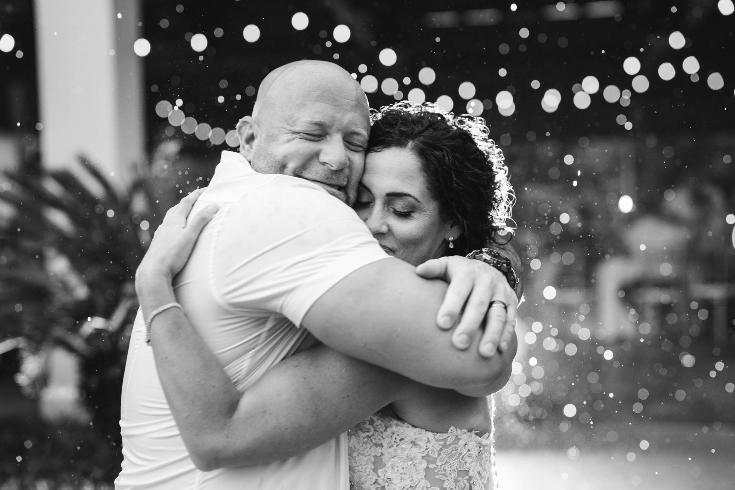 Black-and-white close-up of newlyweds embracing in the rain outside the Lookout Pavilion during their wedding reception.