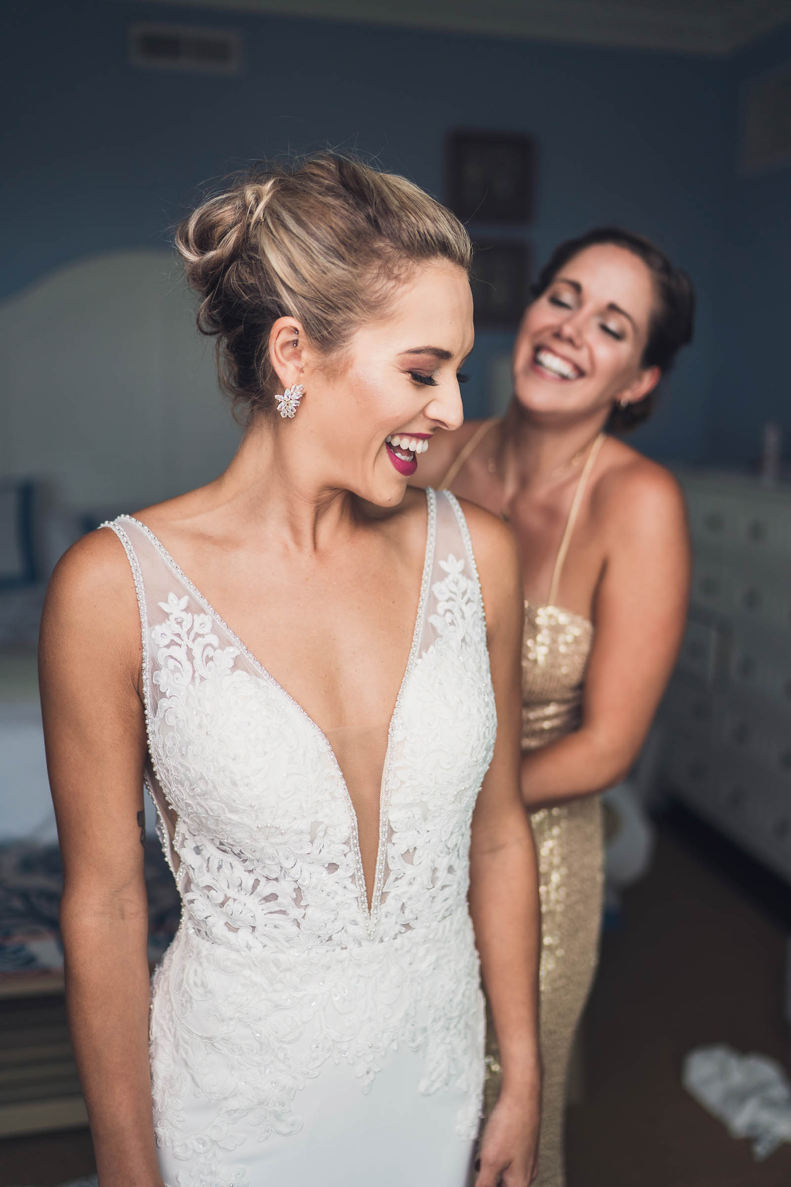 Bride laughs with a friend while getting dressed for her wedding at the Beach Club at Charleston Harbor Resort.