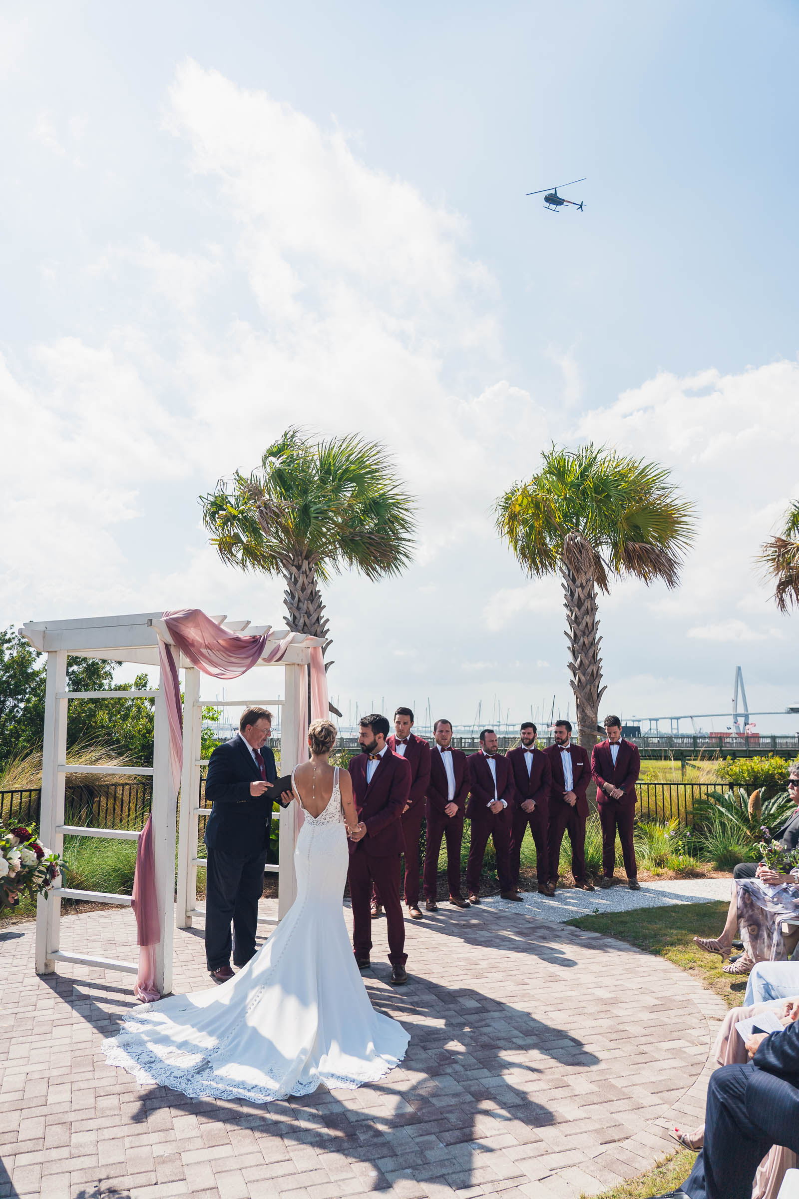 Outdoor wedding ceremony with palm trees, Charleston Harbor, the Ravenel Bridge and a helicopter overhead.
