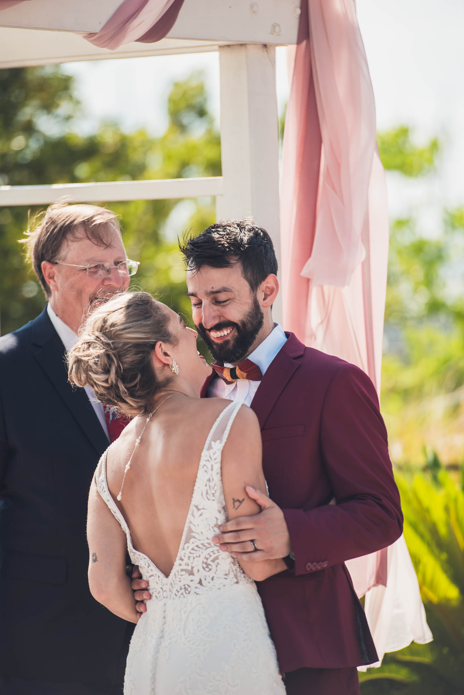 Bride and groom laugh together beneath their wedding arbor immediately after their waterfront ceremony.