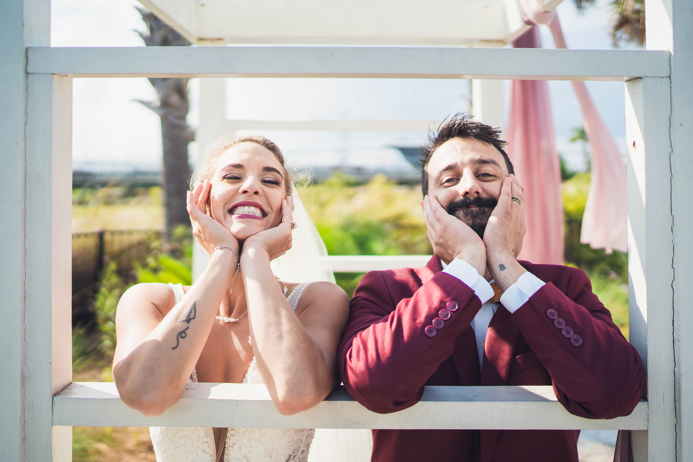 A Proper Wedding Portrait Newlyweds lean through their ceremony arbor and make matching playful poses after their wedding.