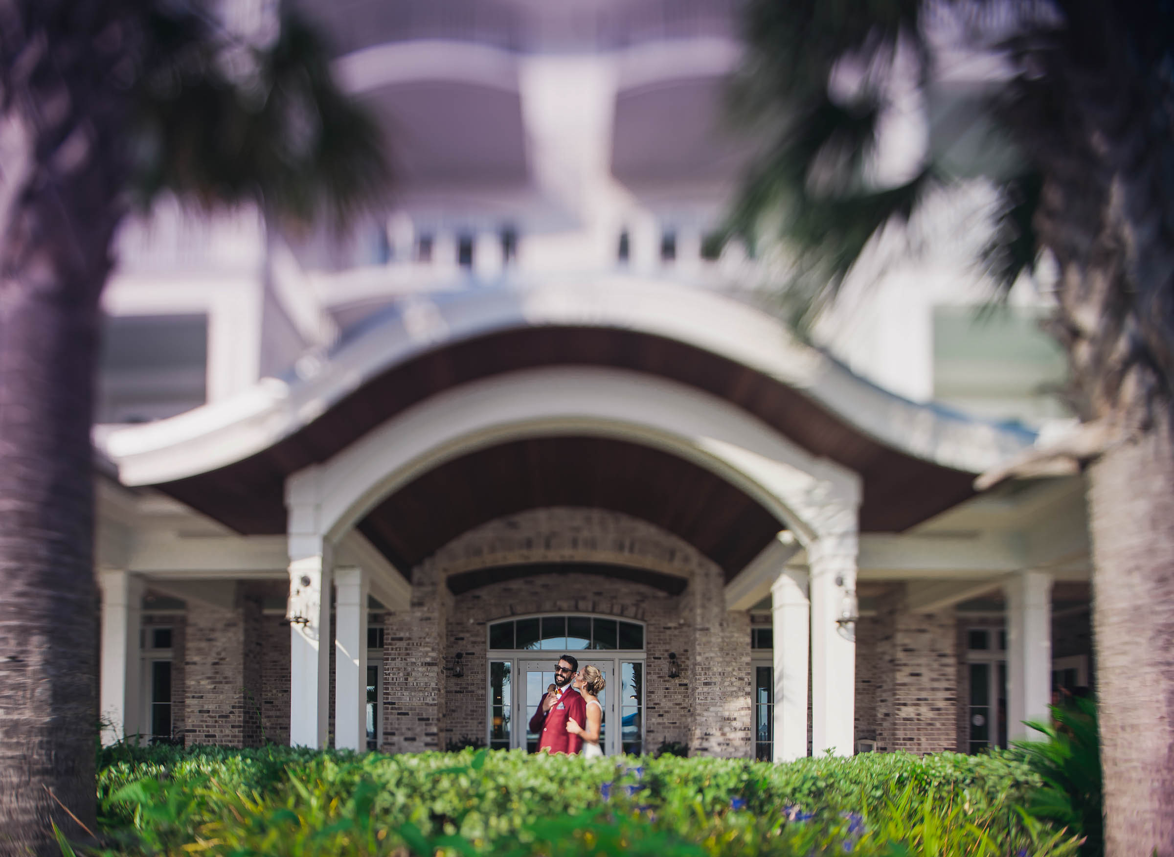 Bride and groom stand together beneath the grand arched entrance of the Beach Club at Charleston Harbor Resort.