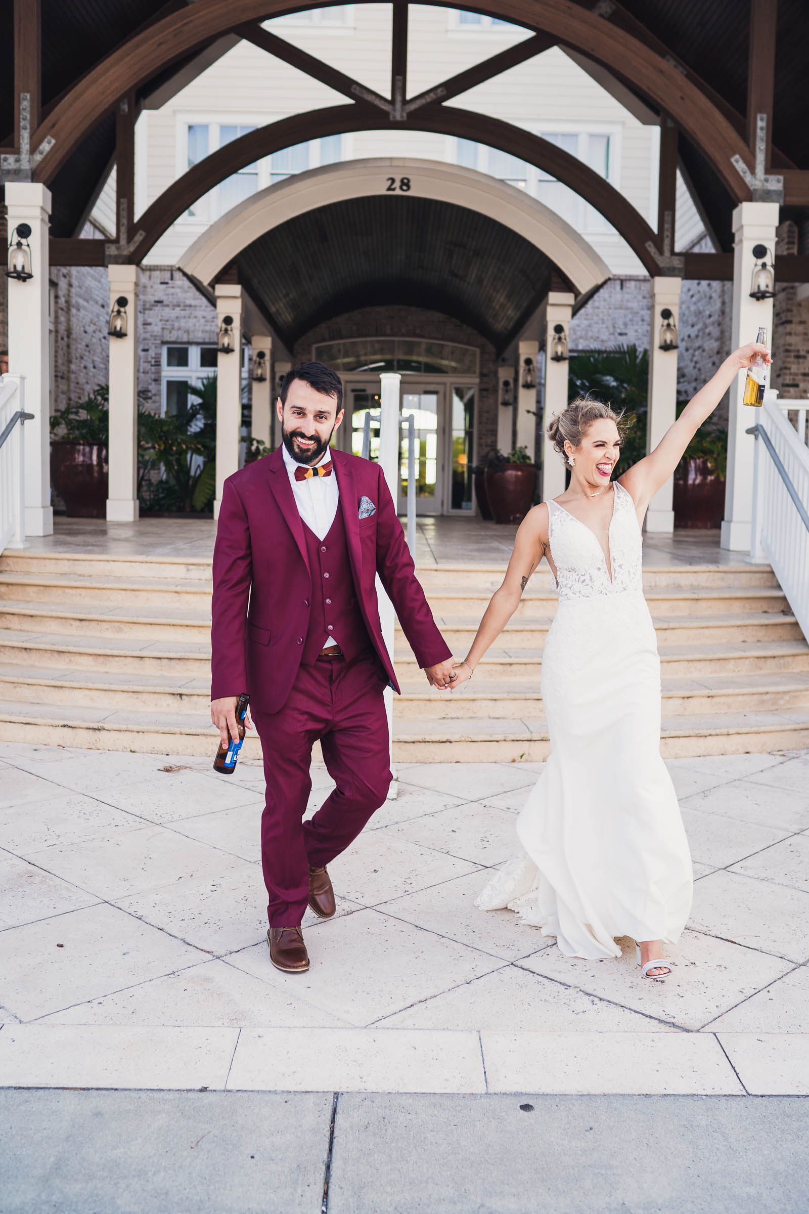 Newlyweds walk hand in hand from the Beach Club entrance carrying beers after their wedding ceremony.