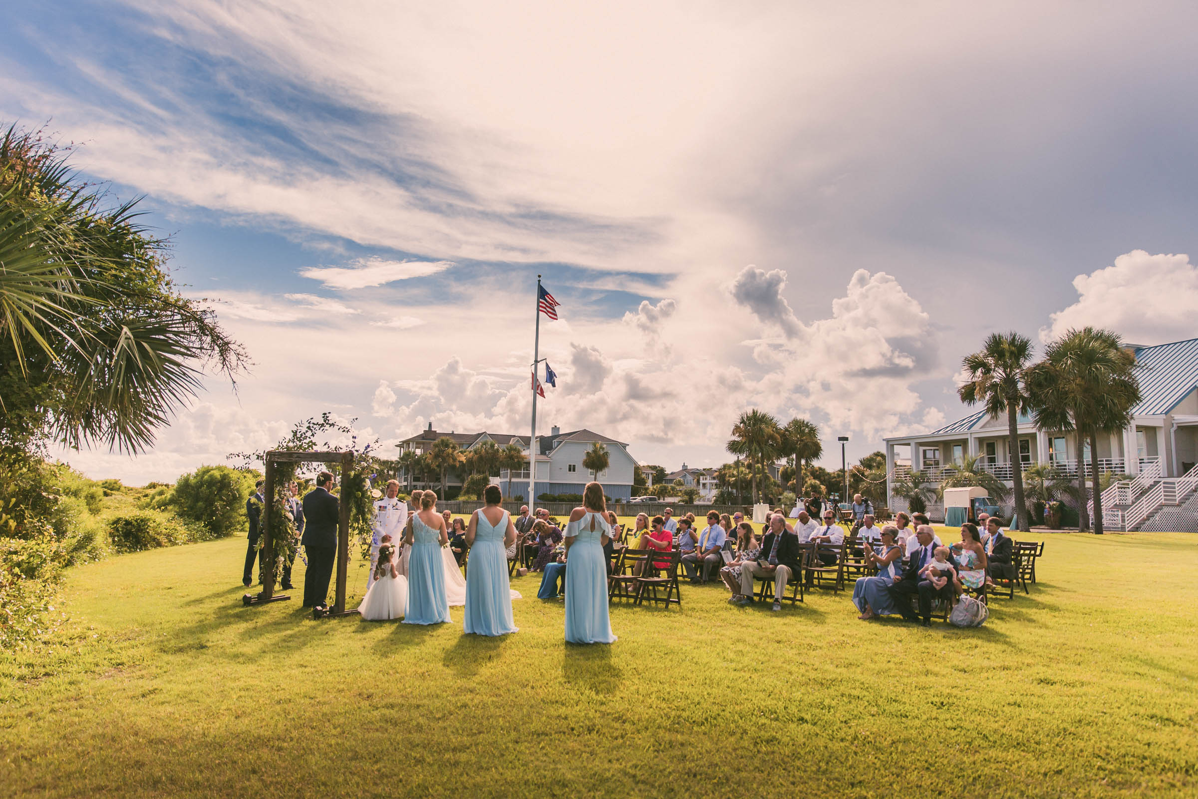 Wide view of an outdoor wedding ceremony on the lawn at Citadel Beach Club on Isle of Palms with guests seated near the beach.