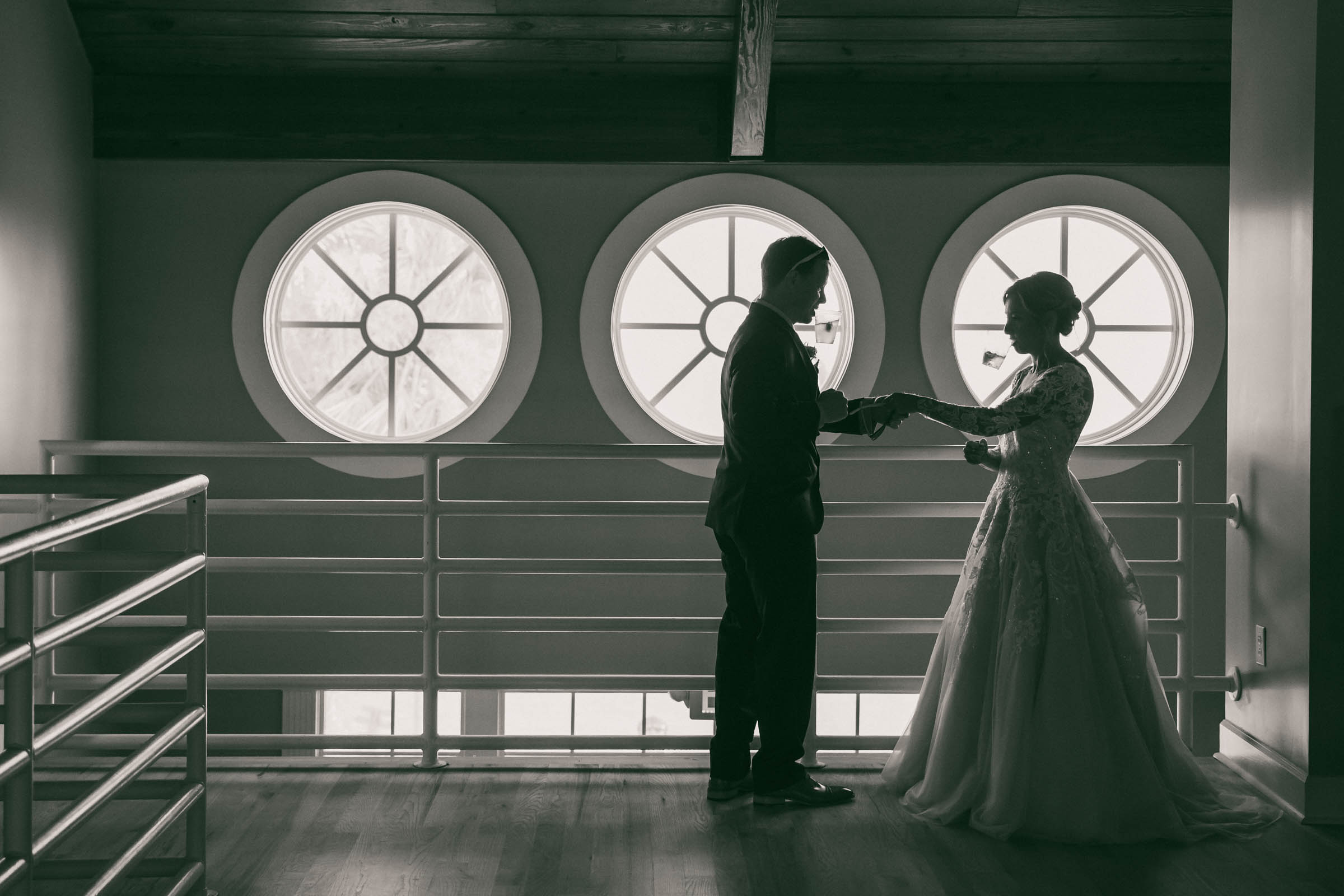 Silhouetted bride and groom holding hands in front of the distinctive round windows inside the Citadel Beach Club on Isle of Palms.