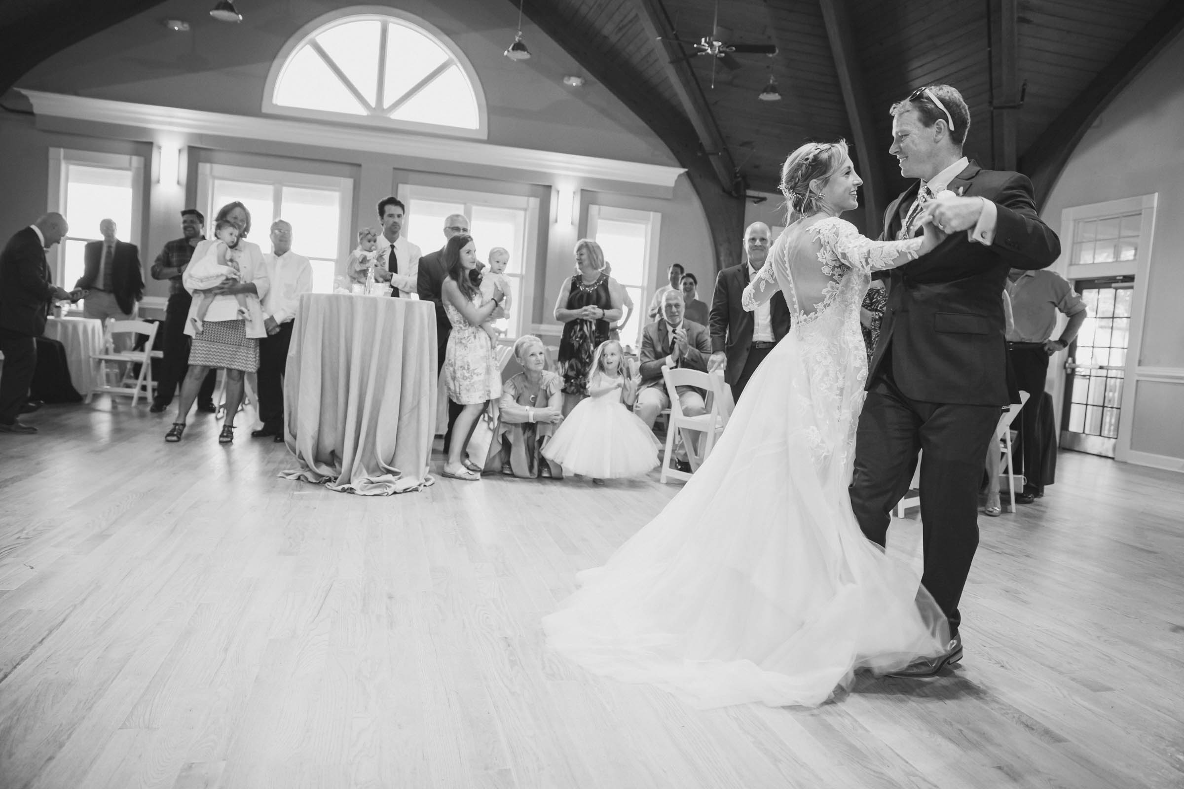 Black-and-white photo of a bride and groom dancing inside the Citadel Beach Club ballroom beneath its high wood ceiling.
