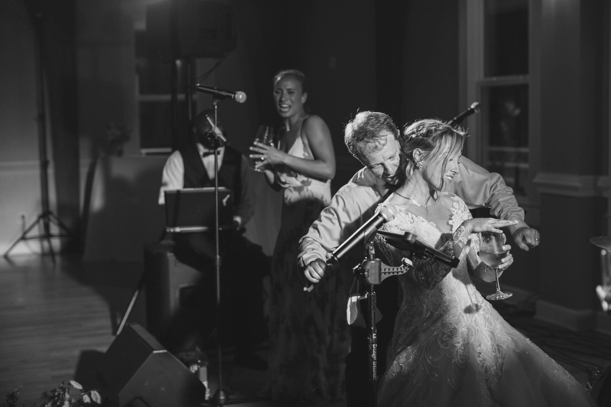 Black-and-white candid of a laughing bride dancing with wedding guests near the band during a Citadel Beach Club reception.
