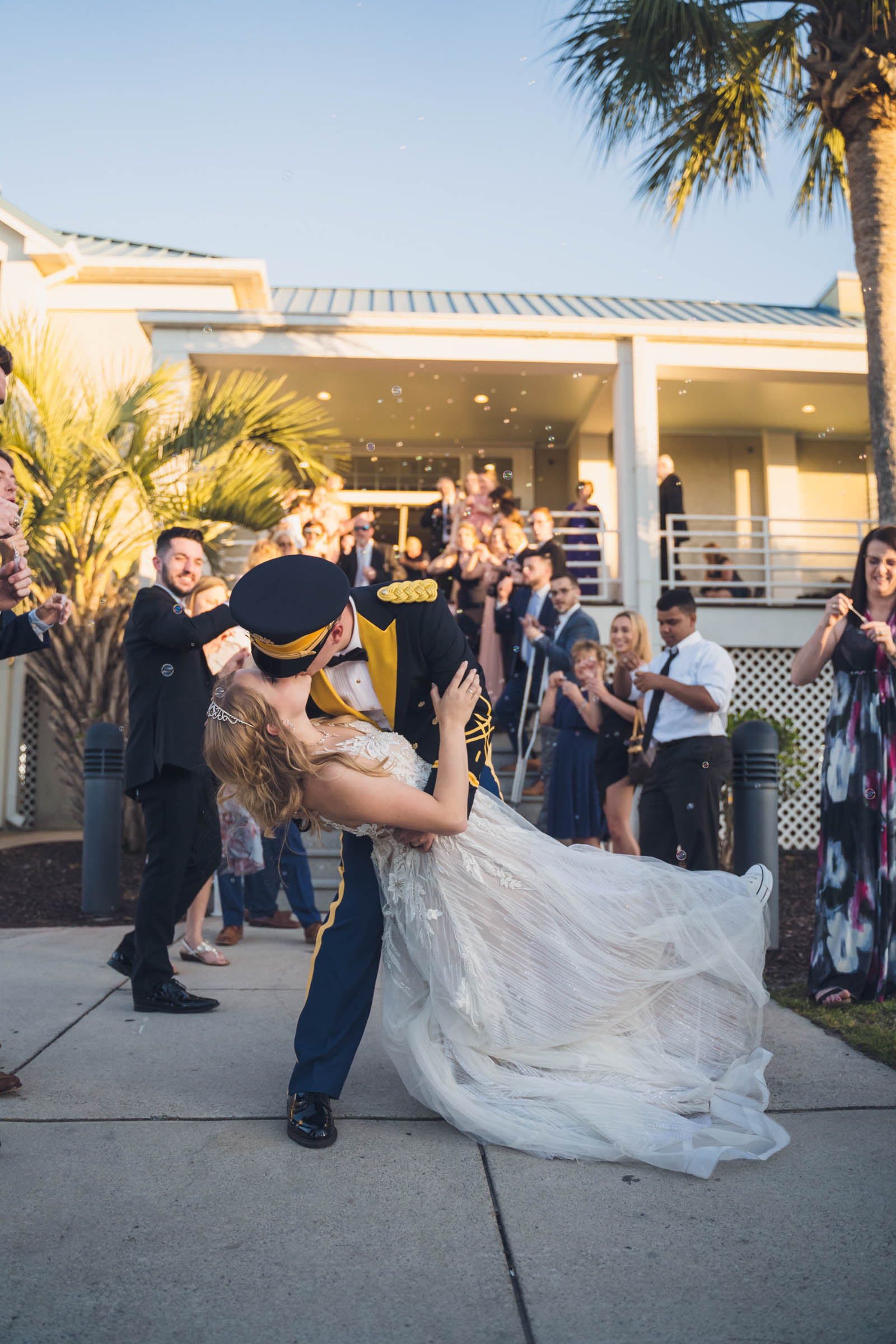 Bride and groom kissing in a dip outside Citadel Beach Club while guests blow bubbles during their wedding exit