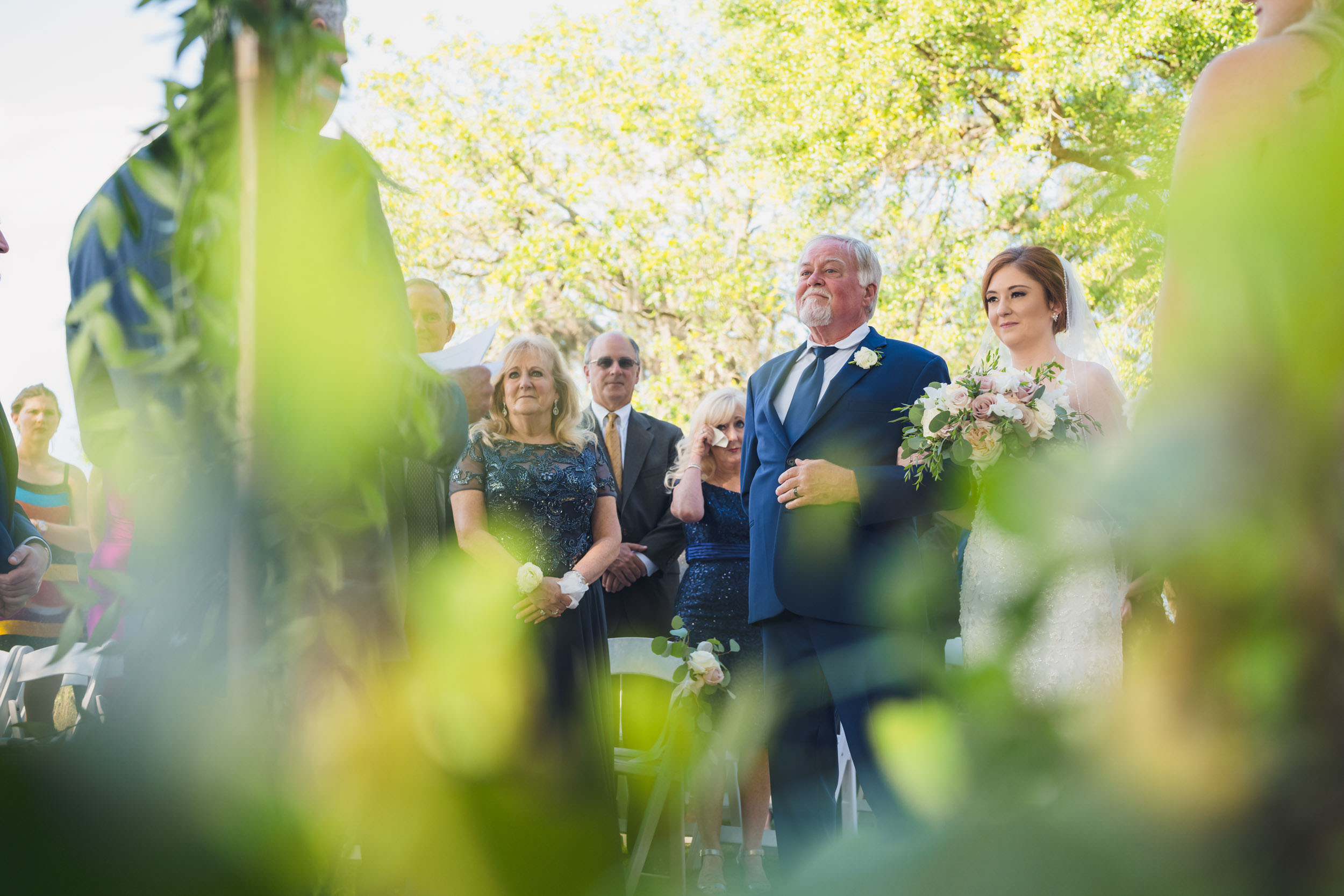 alligator's eye view Bride walking into an outdoor wedding ceremony with her father beneath the trees at Creek Club at I’On in Mount Pleasant.