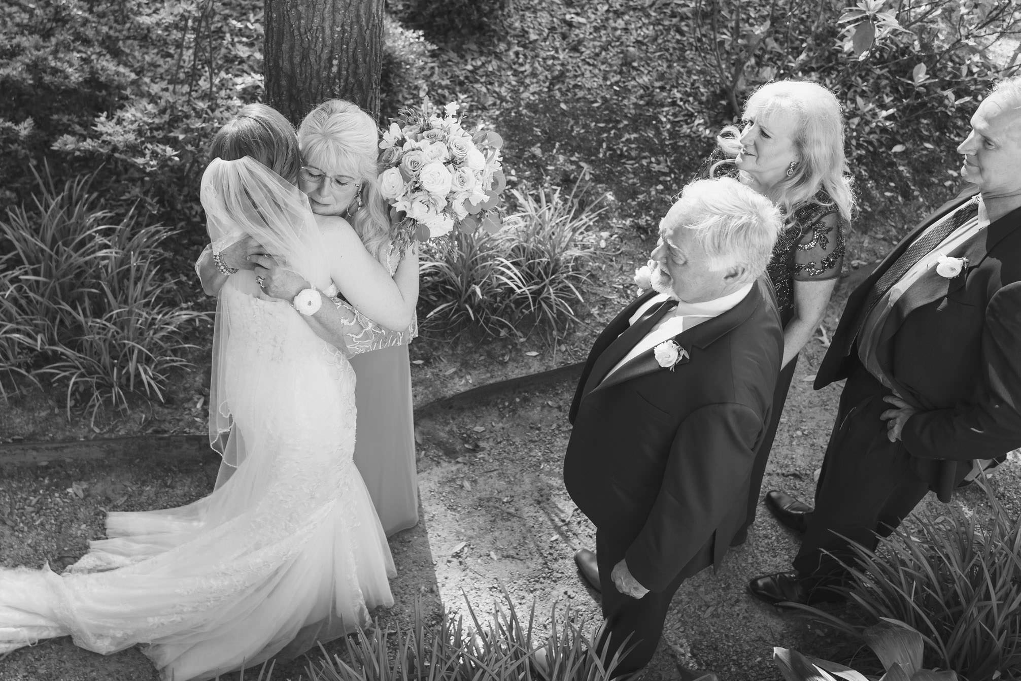 Everybody’s Fine Black-and-white photograph of a bride embracing an emotional family member after an outdoor wedding ceremony at Creek Club at I’On.