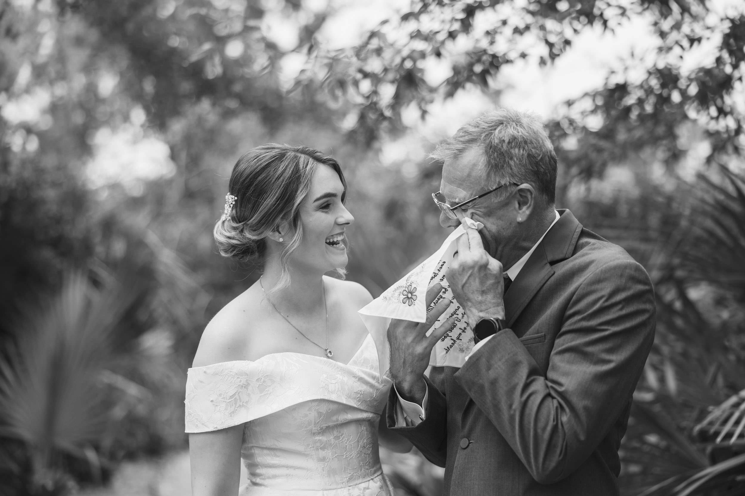 I told you this would happen Black-and-white candid of a bride laughing beside an emotional family member wiping his eyes before a Creek Club at I’On wedding.