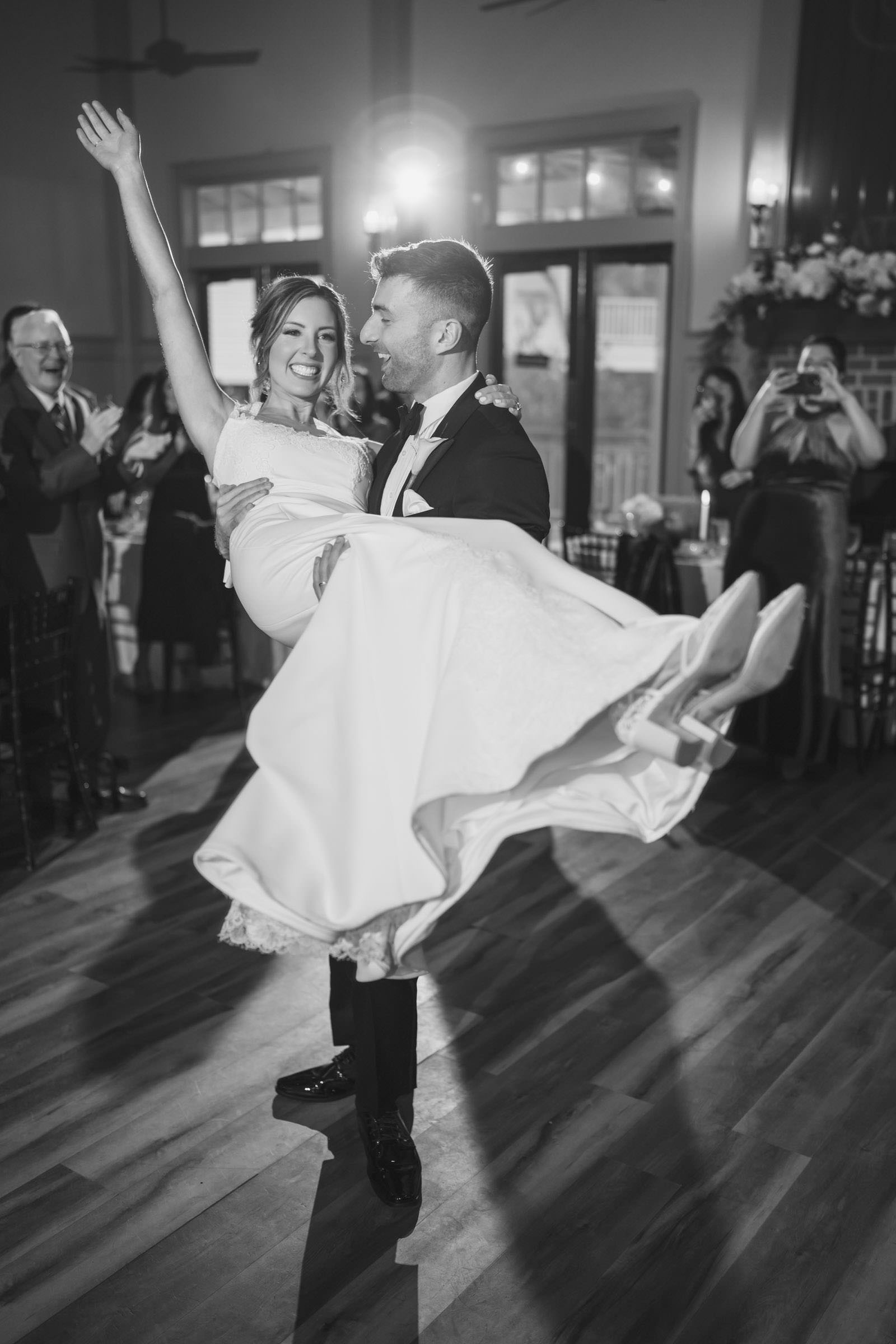 Off Her Feet Black-and-white photo of a groom carrying his bride across the dance floor during a wedding reception at Creek Club at I’On.