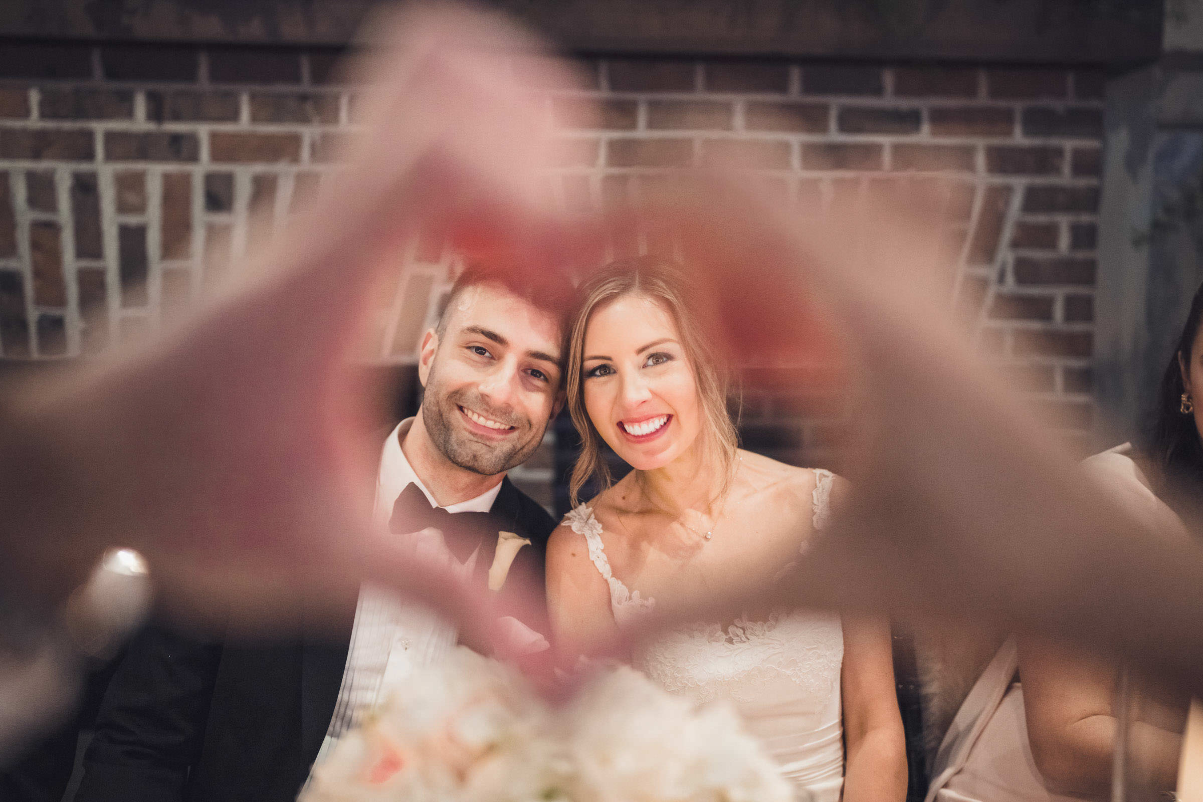heart hands Bride and groom smiling together through a heart shape made by hands during their Creek Club at I’On wedding reception.