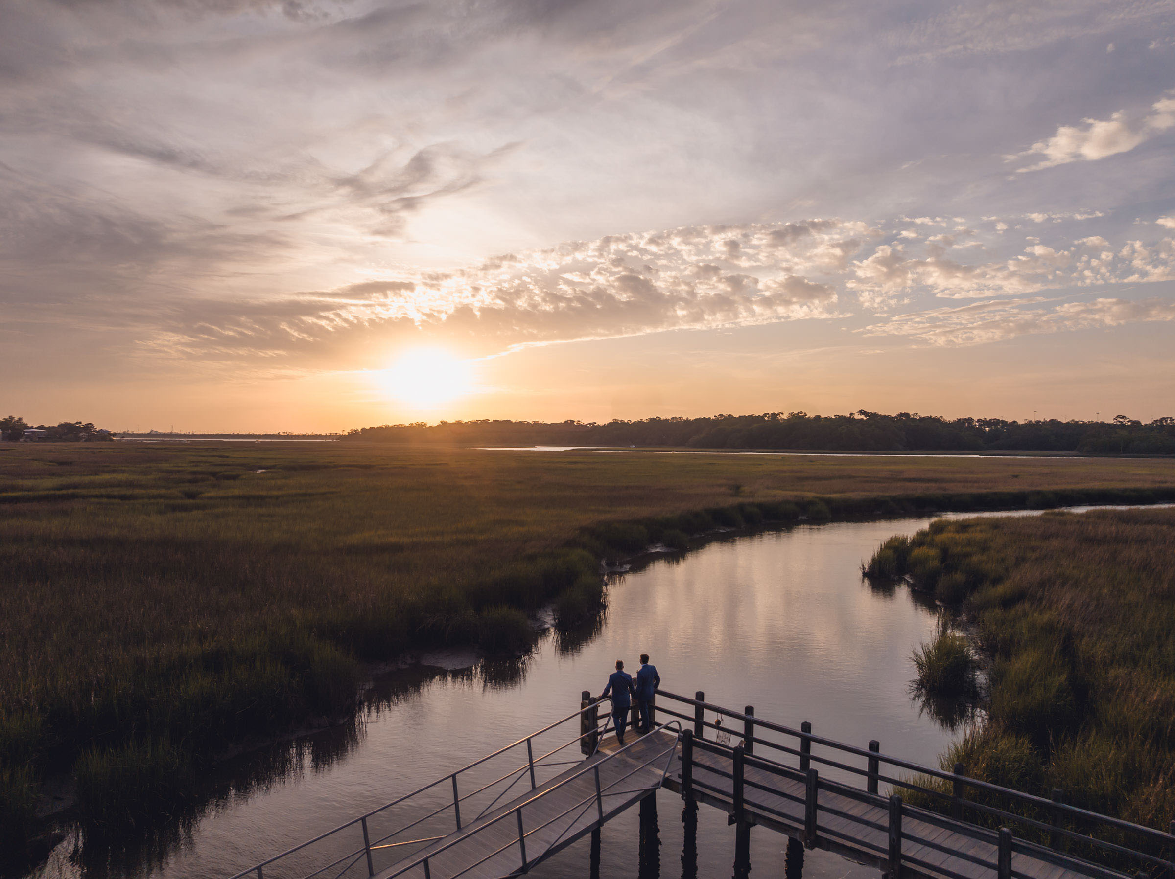 Sunset Appointment Aerial photograph of two grooms standing at the end of the Creek Club at I’On dock during sunset over the Charleston marsh.
