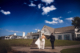 Newlyweds walking hand in hand toward the white clubhouse at Daniel Island Club beneath a bright blue Charleston sky.
