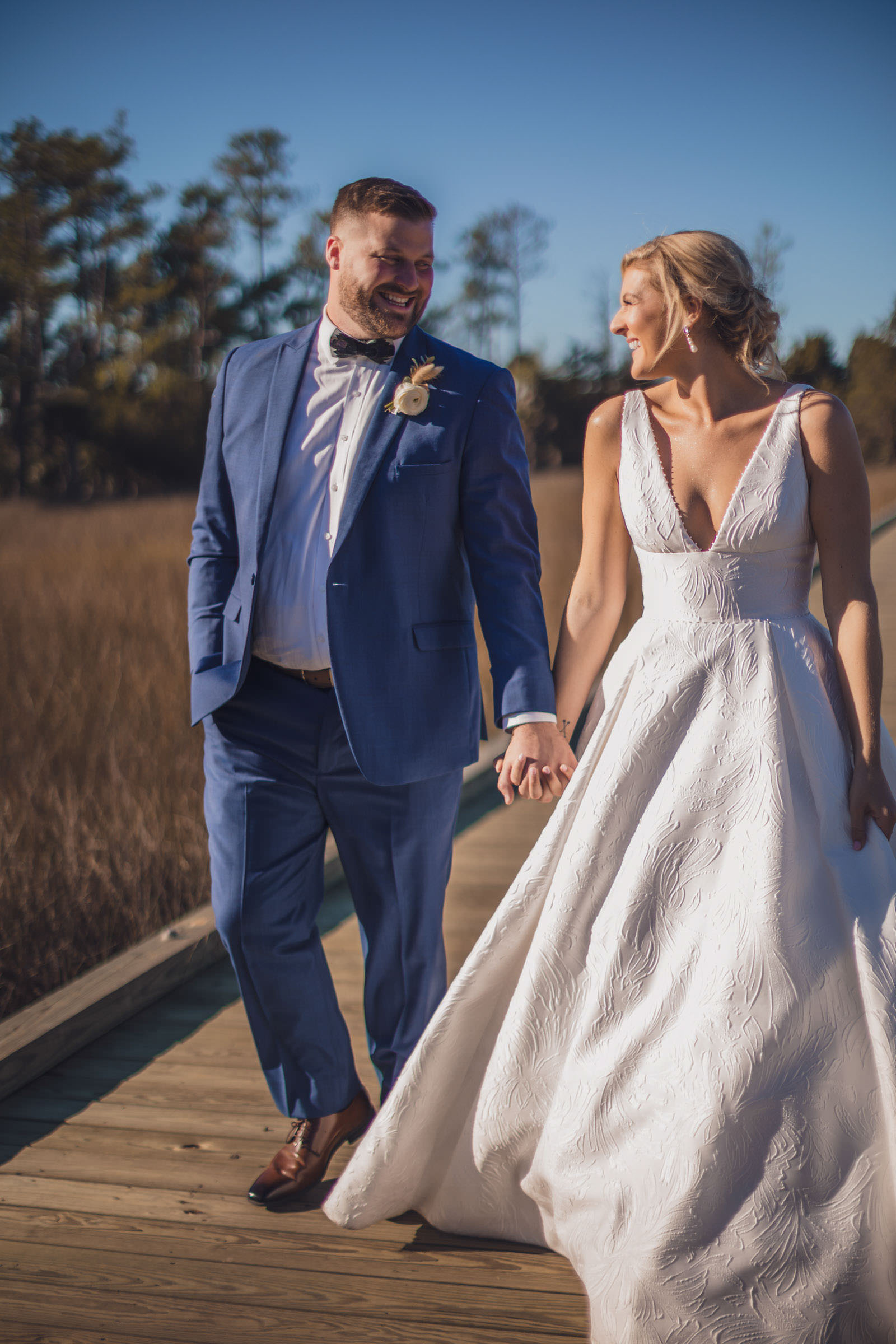 Daniel Island Club Boardwalk Wedding Portrait Bride and groom walking hand in hand along the marsh boardwalk in warm afternoon sunlight.