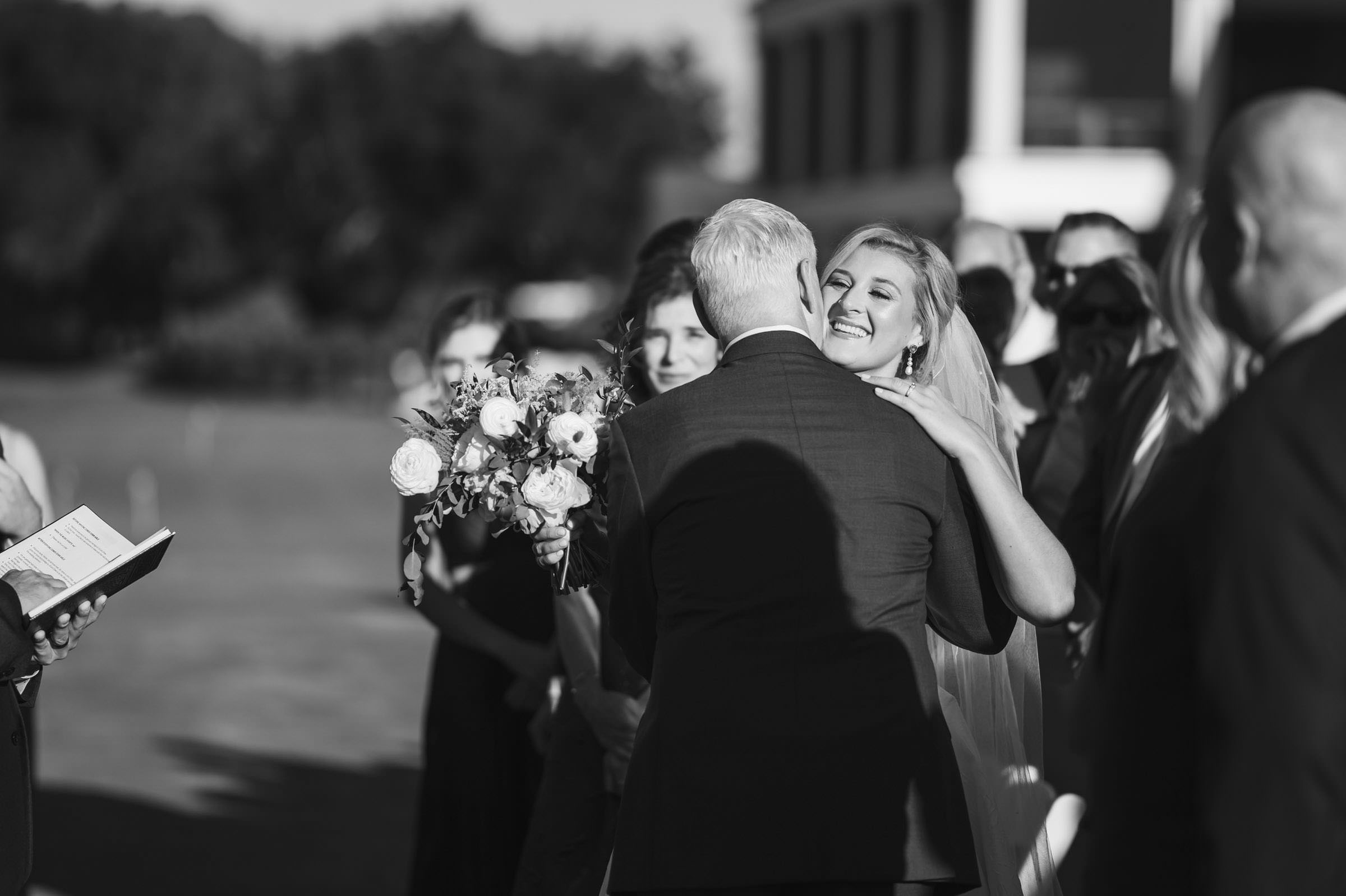 A Very Happy Father of the Bride Black-and-white photograph of the bride smiling while hugging her father during the wedding ceremony.