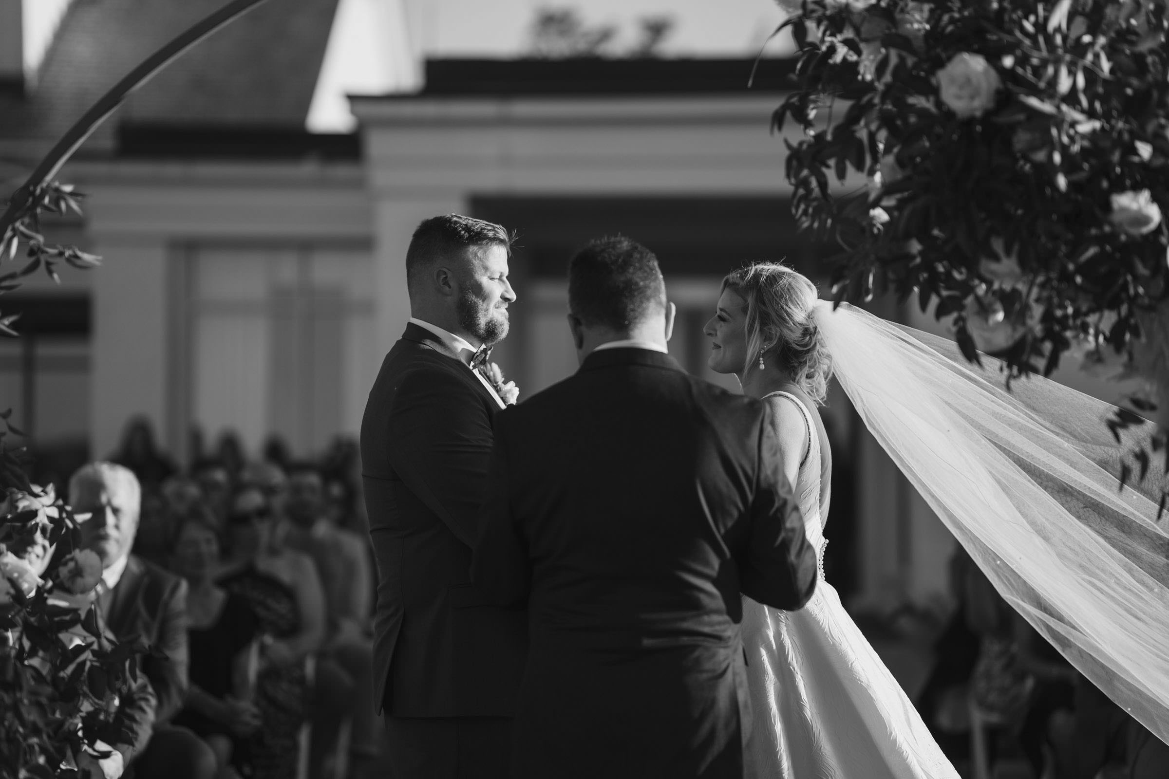Wind in the Veil Black-and-white ceremony photograph of the bride and groom with her long veil blowing dramatically in the wind.