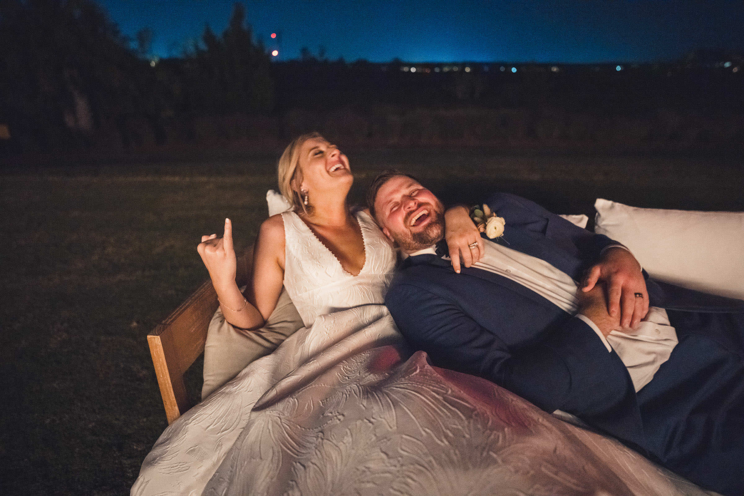 Married and Cracking Up Bride and groom laughing together on an outdoor sofa after dark during their Daniel Island Club wedding reception.