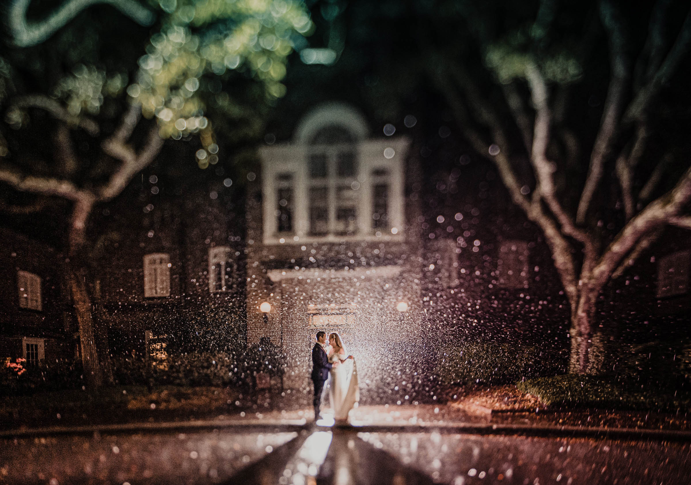 Rainy Night Portrait at the Historic Rice Mill Bride and groom stand together in the rain outside the brick Historic Rice Mill beneath glowing courtyard lights.