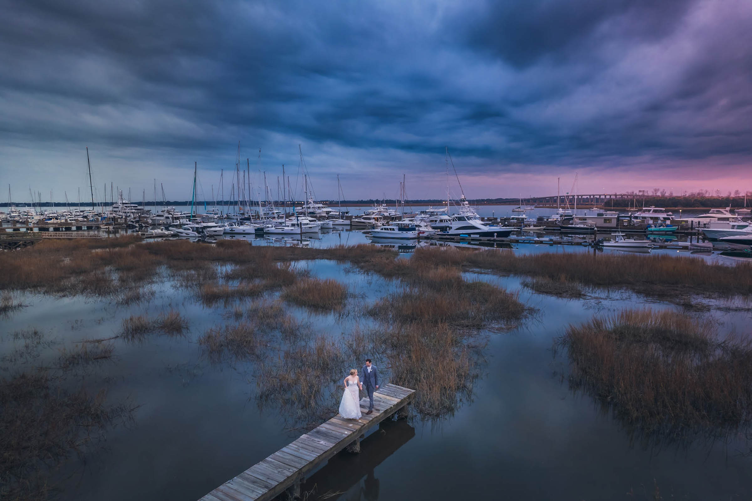 Historic Rice Mill Waterfront Wedding Aerial Aerial view of newlyweds standing on a dock beside the marsh and Charleston City Marina near the Historic Rice Mill.