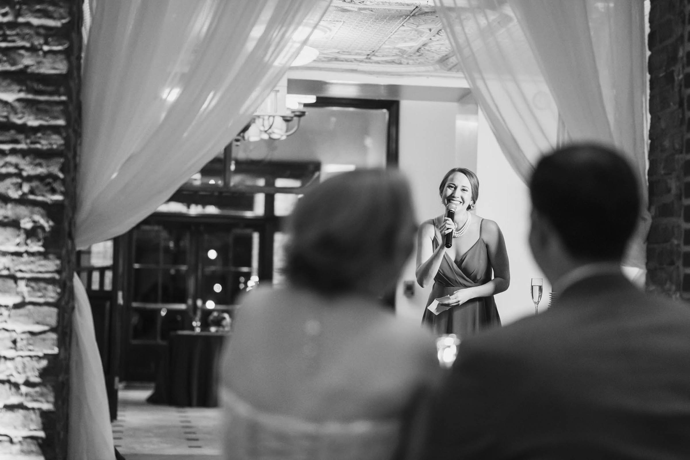 Wedding Toast at the Historic Rice Mill Bridesmaid gives a wedding toast framed by brick walls and draped fabric inside the Historic Rice Mill reception.