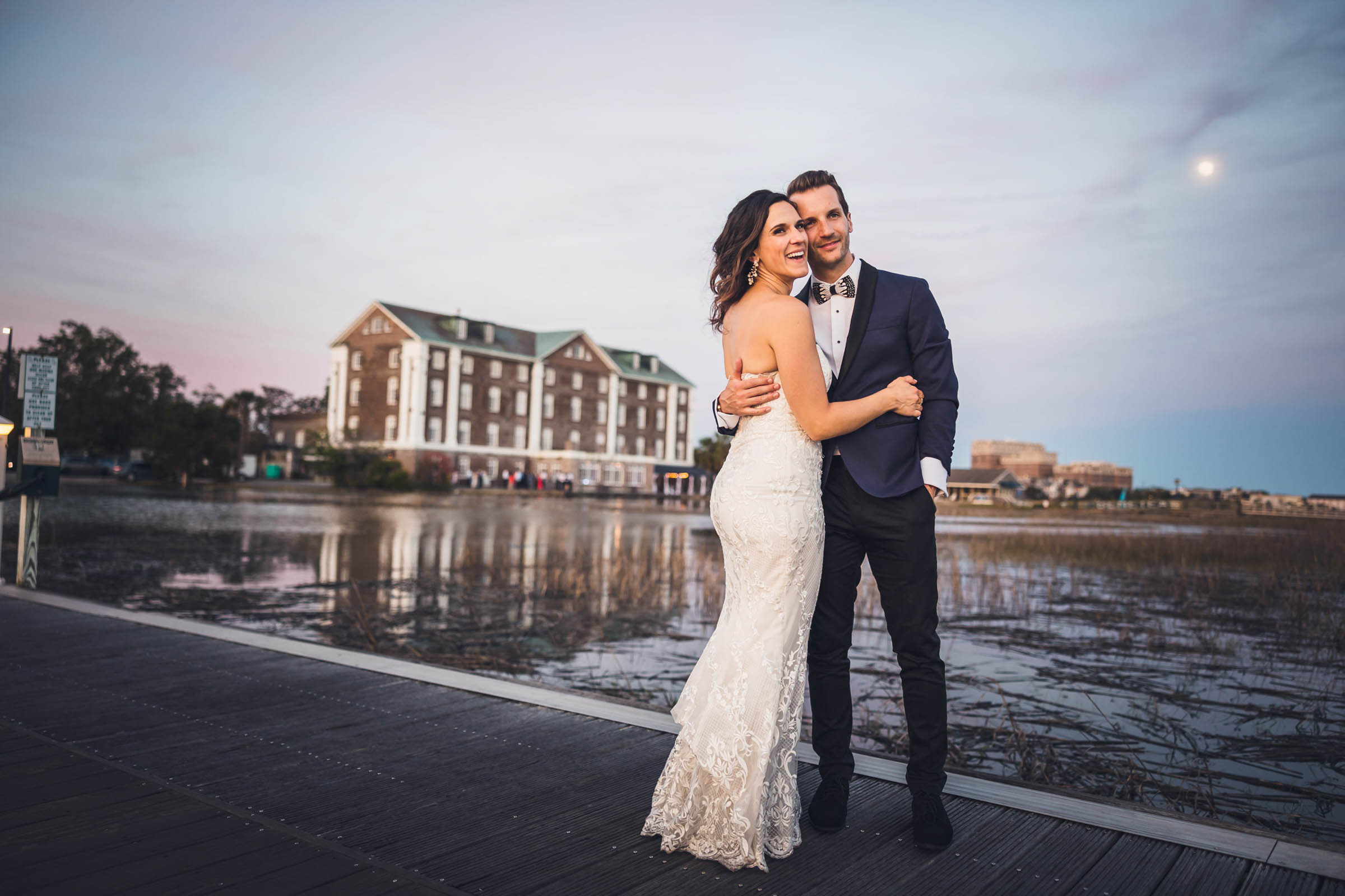 Charleston Waterfront Wedding Portrait Bride and groom pose along the waterfront near the Historic Rice Mill with the marina and Charleston skyline behind them.