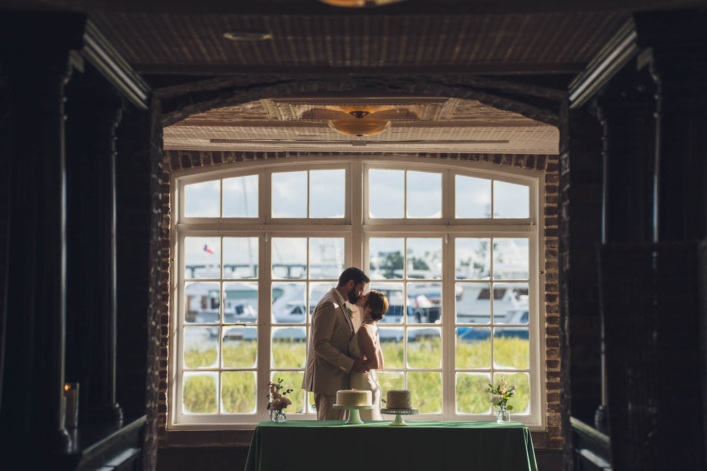 Historic Rice Mill Marina Window Portrait Bride and groom kiss in silhouette before a large window overlooking the marina at the Historic Rice Mill.