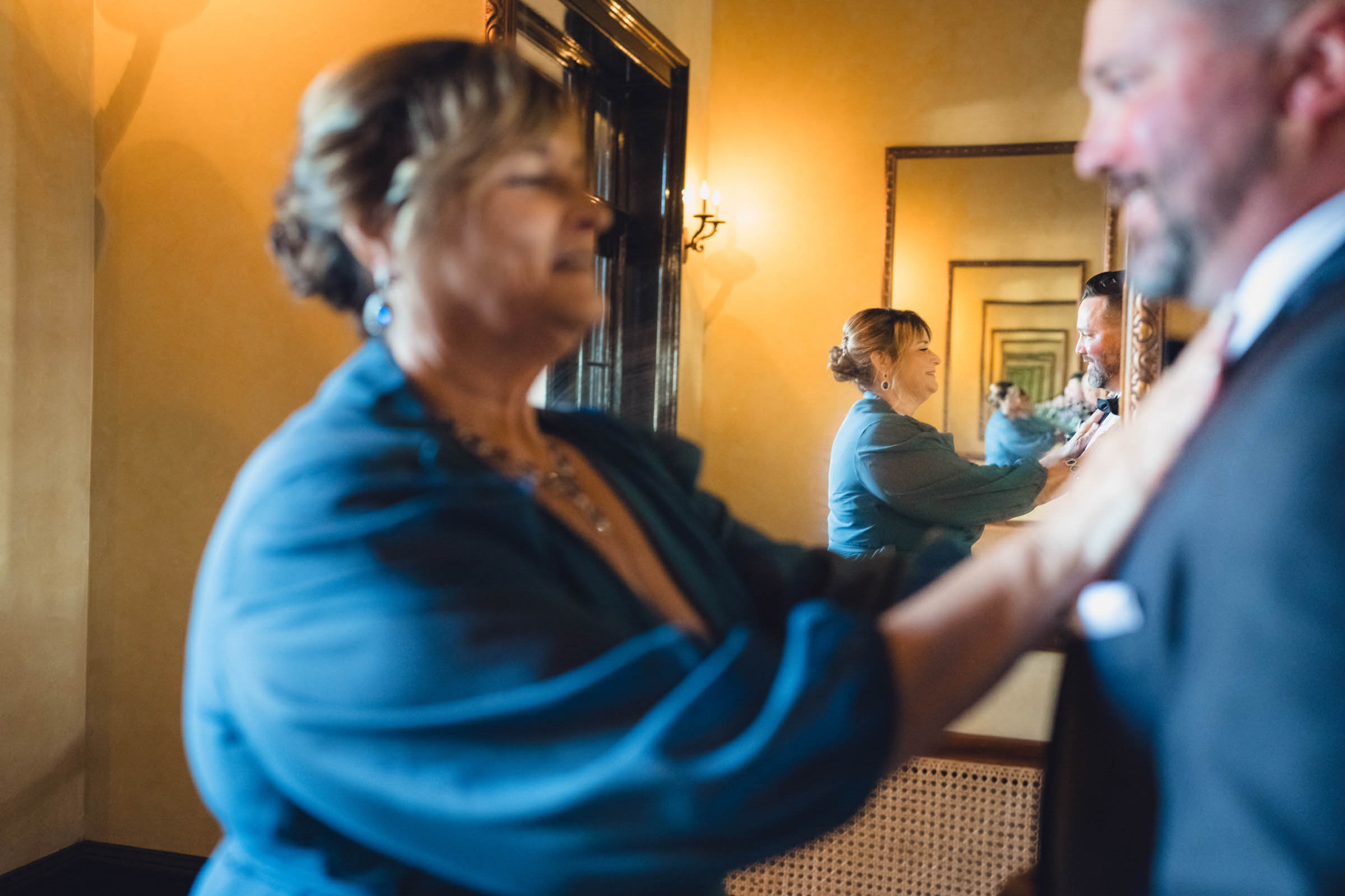 Getting Ready at the Historic Rice Mill A family member adjusts the groom's jacket in a warm mirrored room before a Historic Rice Mill wedding.