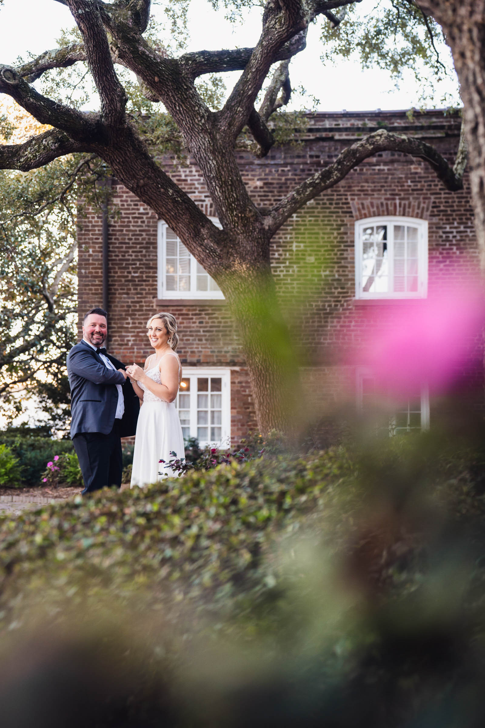 Historic Rice Mill Live Oak First Look Bride and groom stand beneath a sprawling live oak beside the historic brick exterior of the Rice Mill.