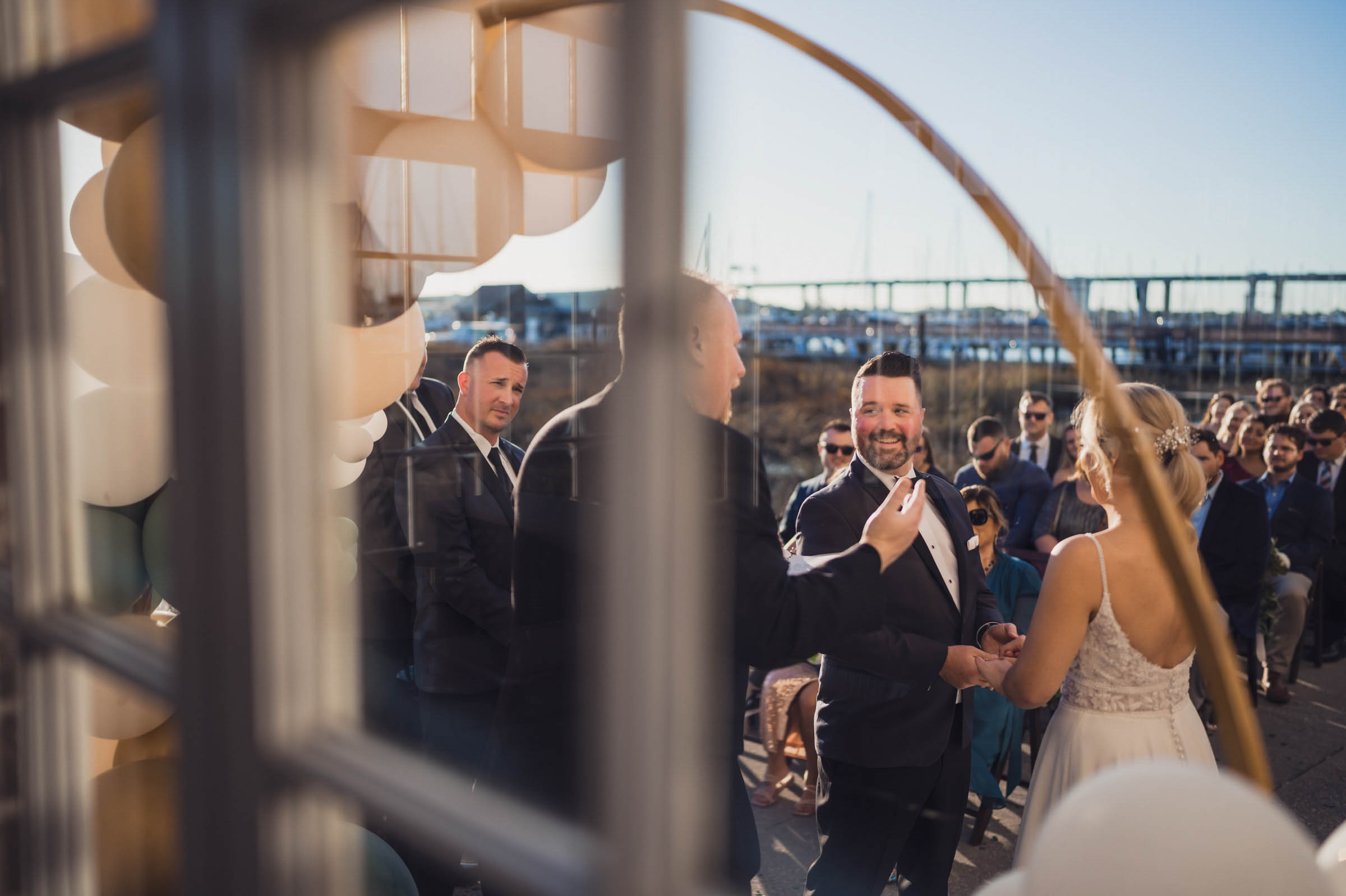 Historic Rice Mill Waterfront Ceremony Groom looks toward his bride during an outdoor wedding ceremony beside the marina at the Historic Rice Mill.