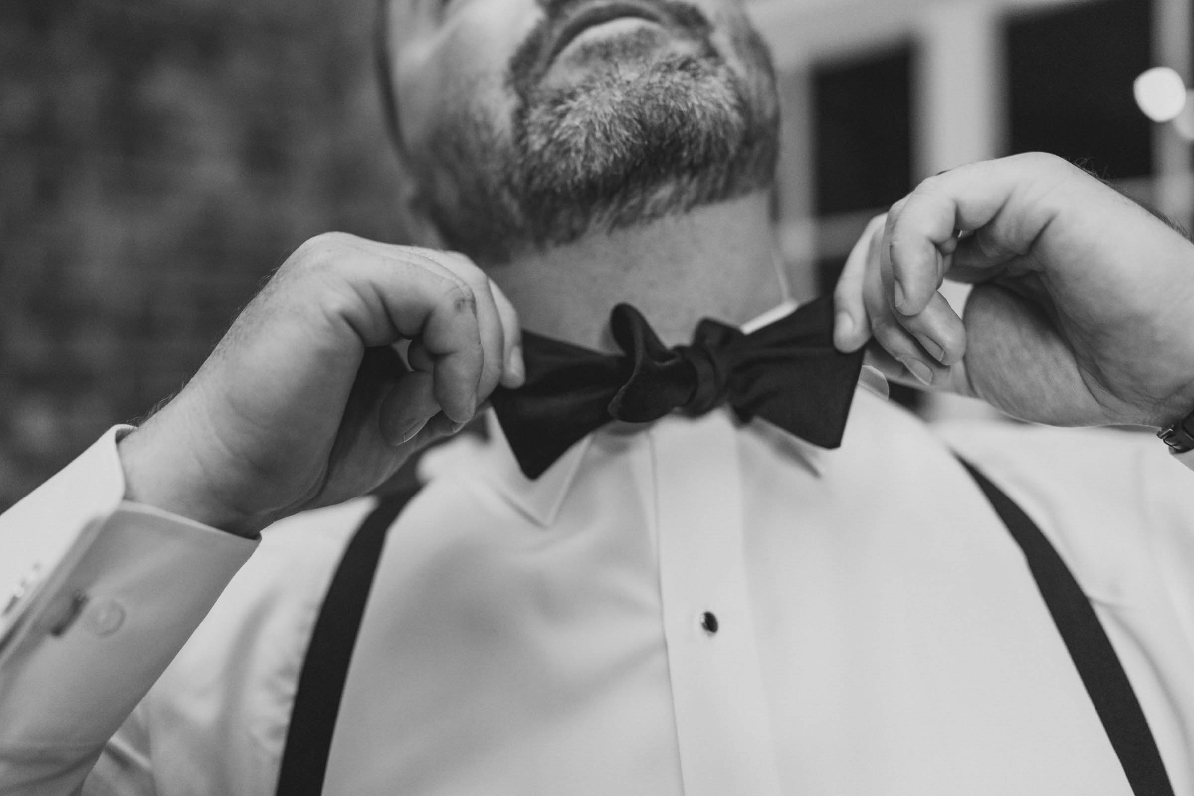 Groom Getting Ready at the Historic Rice Mill Black-and-white close-up of a groom adjusting his bow tie and suspenders before his Historic Rice Mill wedding.