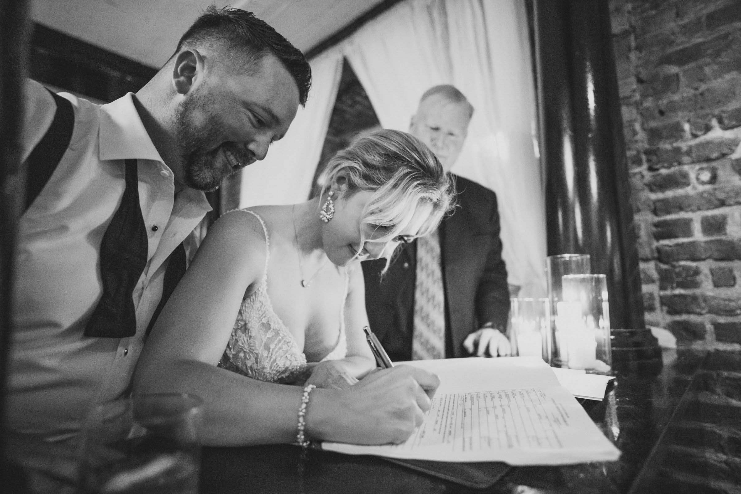 Signing the Marriage License at the Historic Rice Mill Bride signs the marriage license while the groom smiles beside her during their Historic Rice Mill wedding.