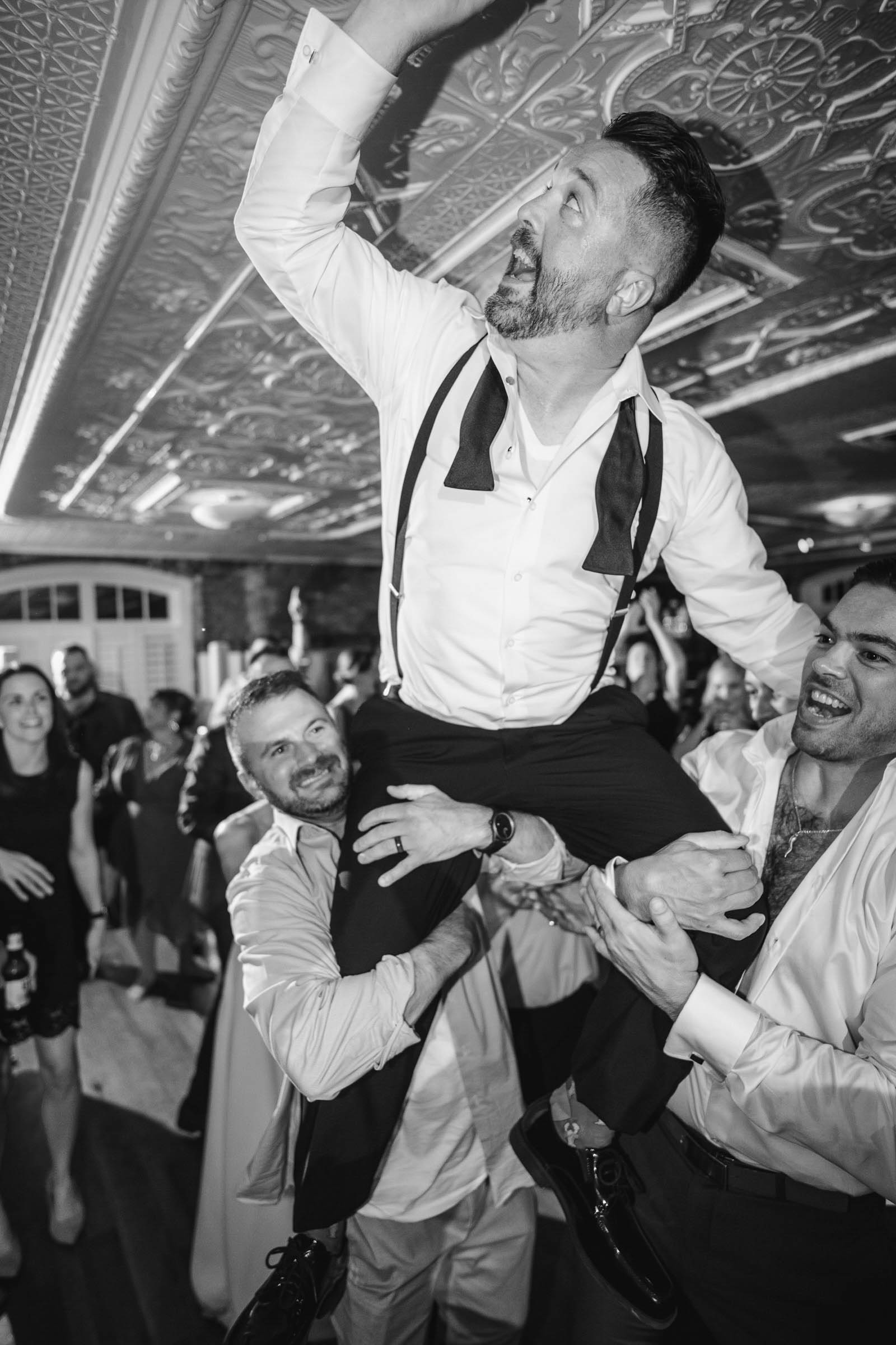 Historic Rice Mill Wedding Reception Dance Floor Groom is lifted onto friends' shoulders during a lively black-and-white wedding reception at the Historic Rice Mill.