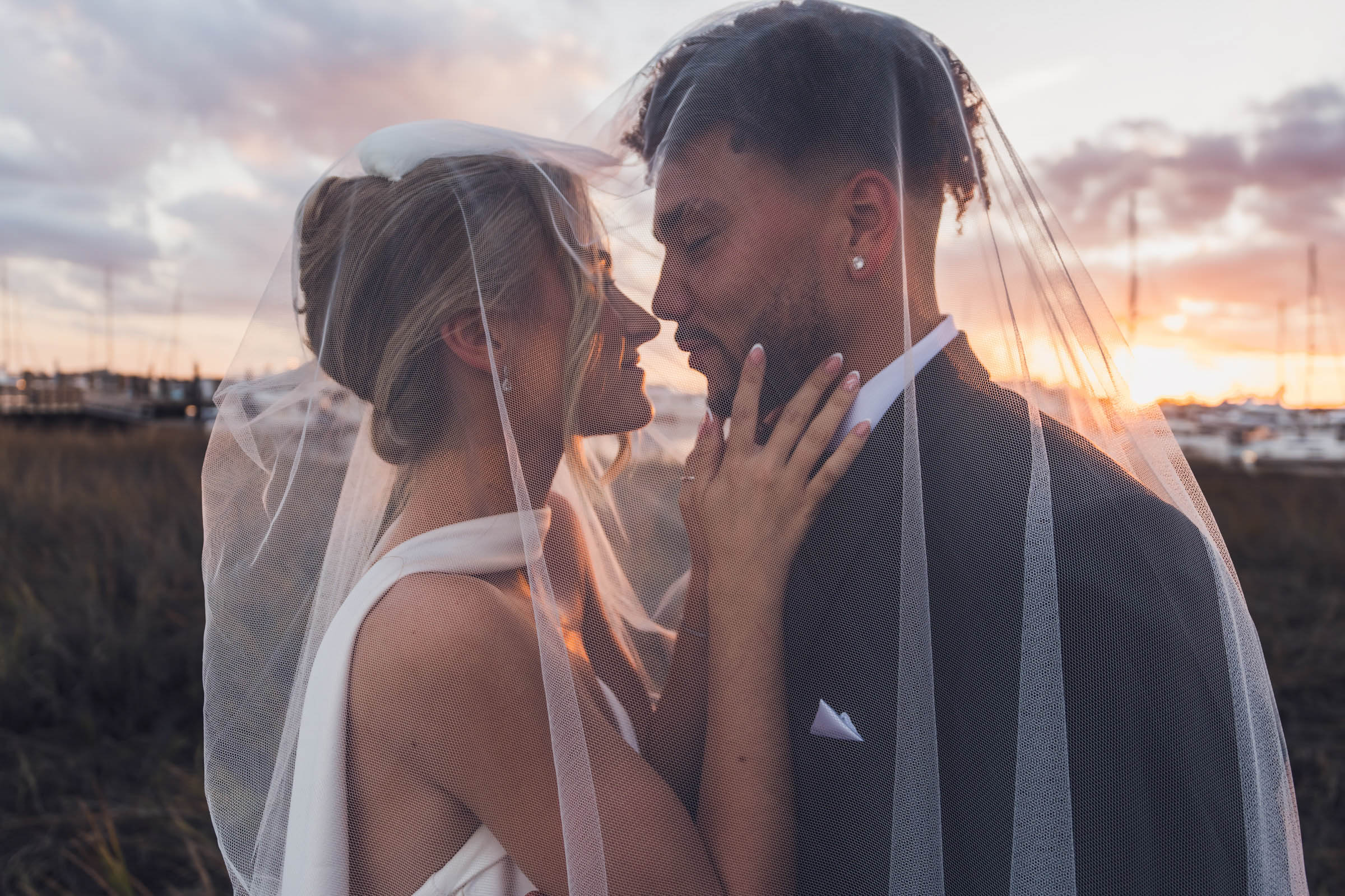 Sunset Veil Portrait at the Historic Rice Mill Bride and groom share an intimate portrait beneath her veil with the marina sunset glowing behind them.