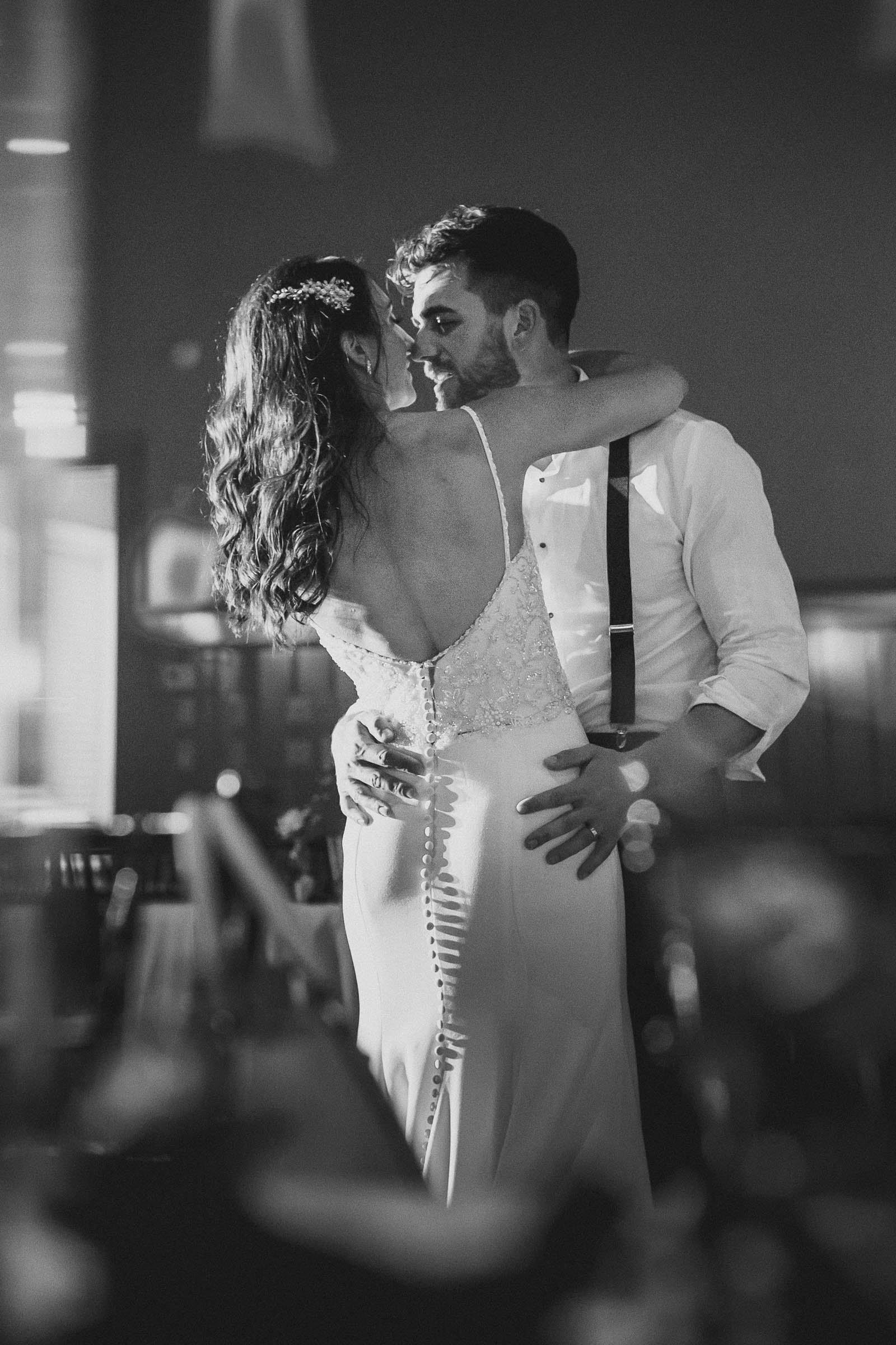 Bride and groom sharing an intimate slow dance during the reception, backlit in soft light—romantic black and white wedding moment.