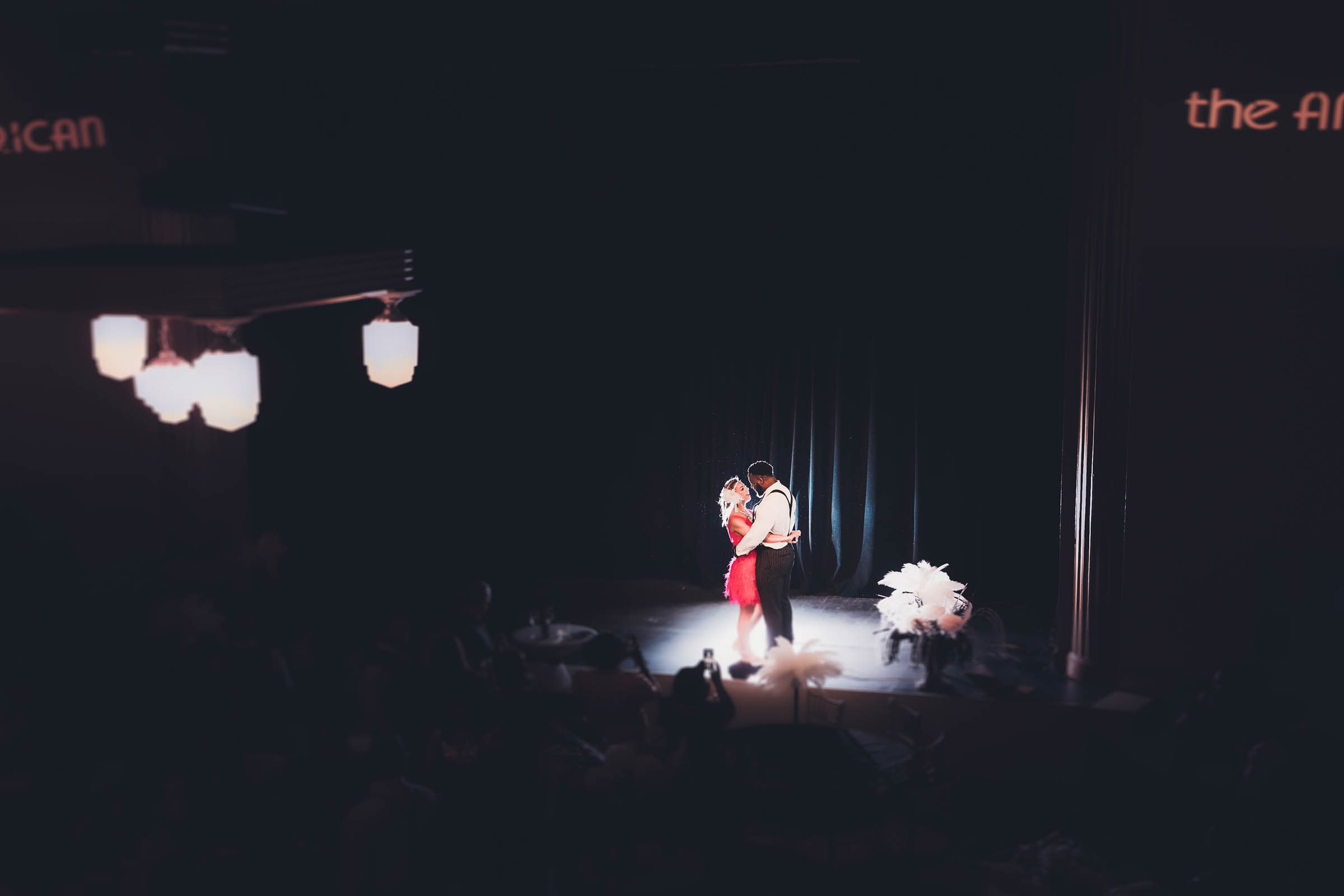 Couple sharing a dramatic first dance on a dimly lit stage under a spotlight—moody, cinematic wedding reception moment.