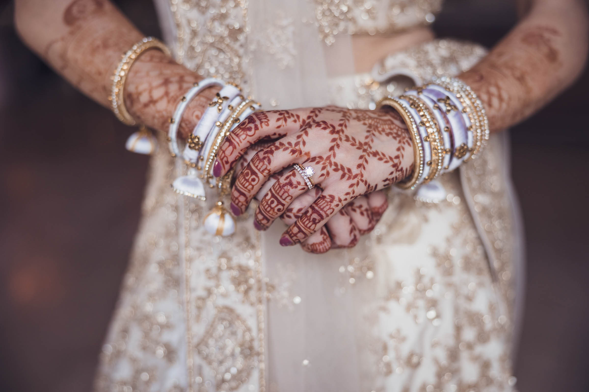 Close-up of bride’s hands with intricate henna designs, bangles, and engagement ring—detailed Indian wedding portrait.