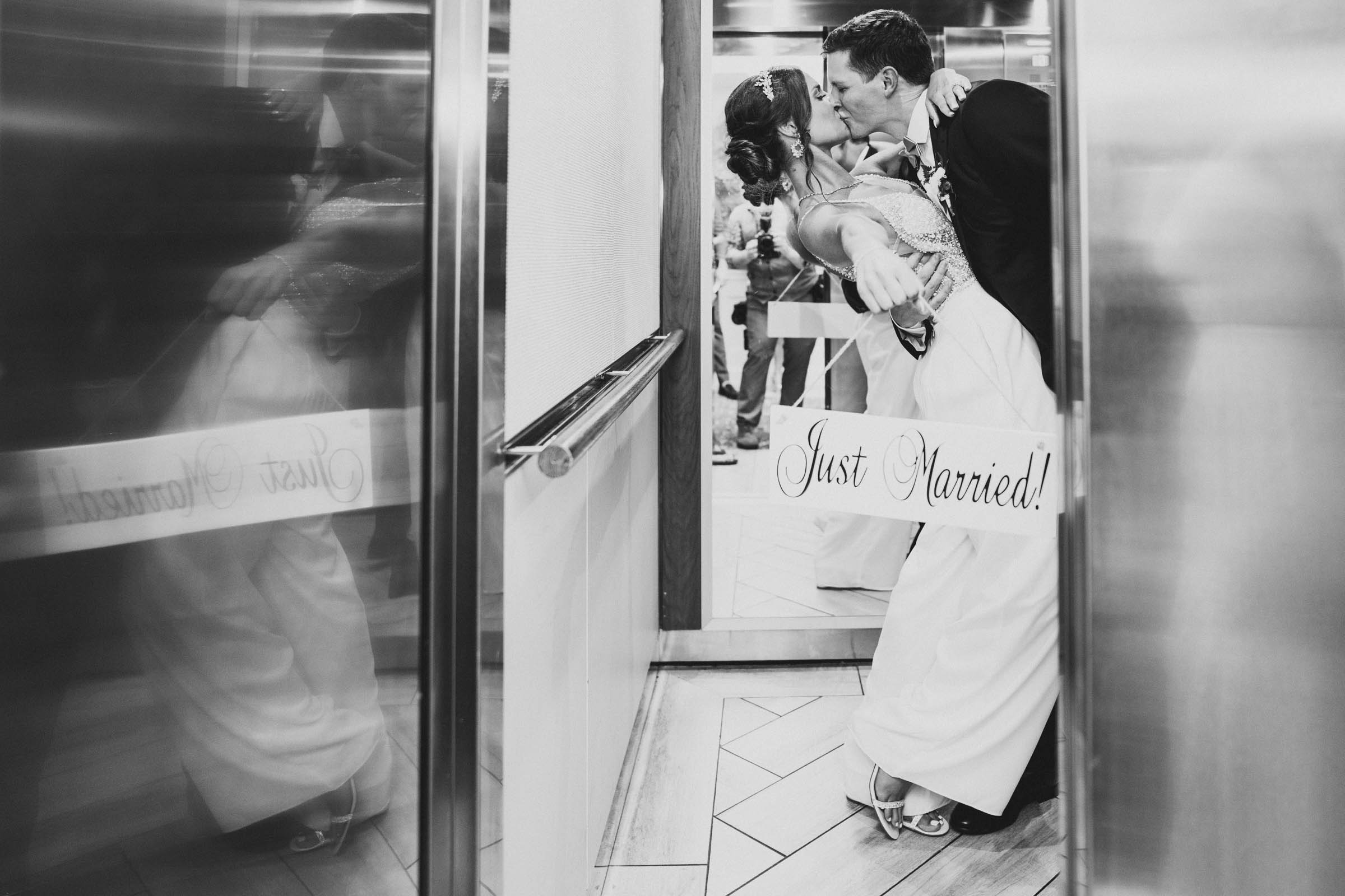 The couple kisses in the elevator holding a Just Married sign in a playful black and white portrait at Wild Dunes Resort near Charleston, South Carolina.