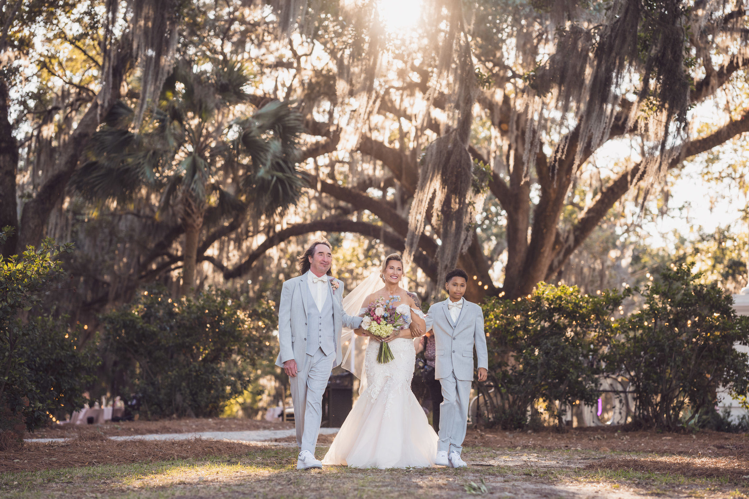Bride walking down outdoor aisle under oak trees with Spanish moss at Admiral’s House Riverfront Park wedding