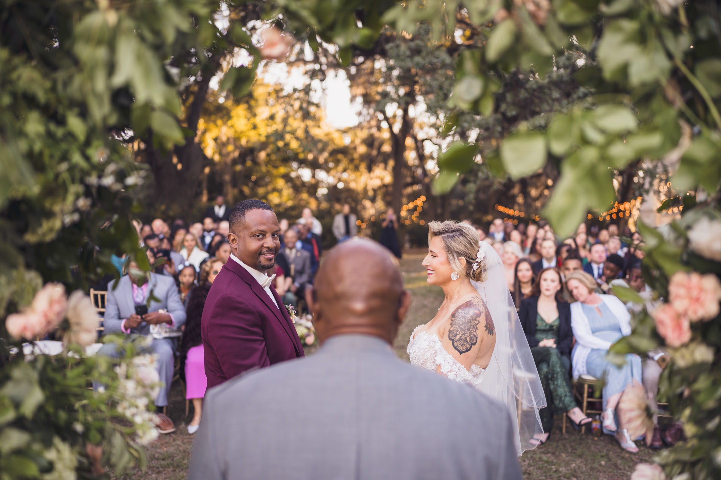 Outdoor wedding ceremony at Admiral’s House framed by greenery and floral arch with guests seated