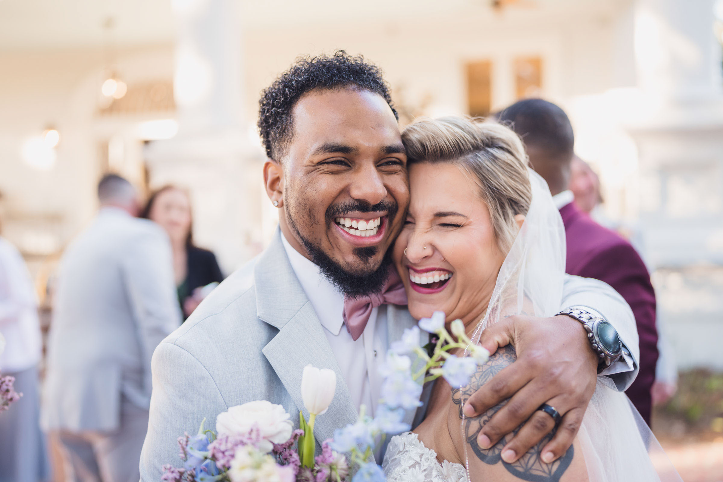 Close-up candid of bride and groomsman laughing and hugging during wedding day at Admiral’s House